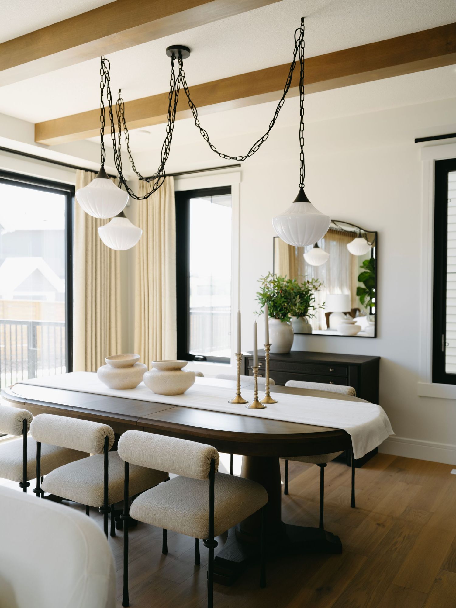 Modern dining room with dark wood table, upholstered chairs, globe pendant lights, exposed beams, and black sideboard.