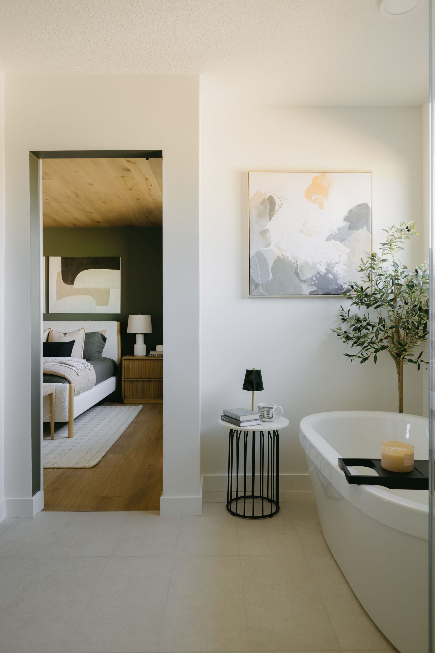 Spa-like ensuite with freestanding tub, olive tree, abstract art, and view into green bedroom.