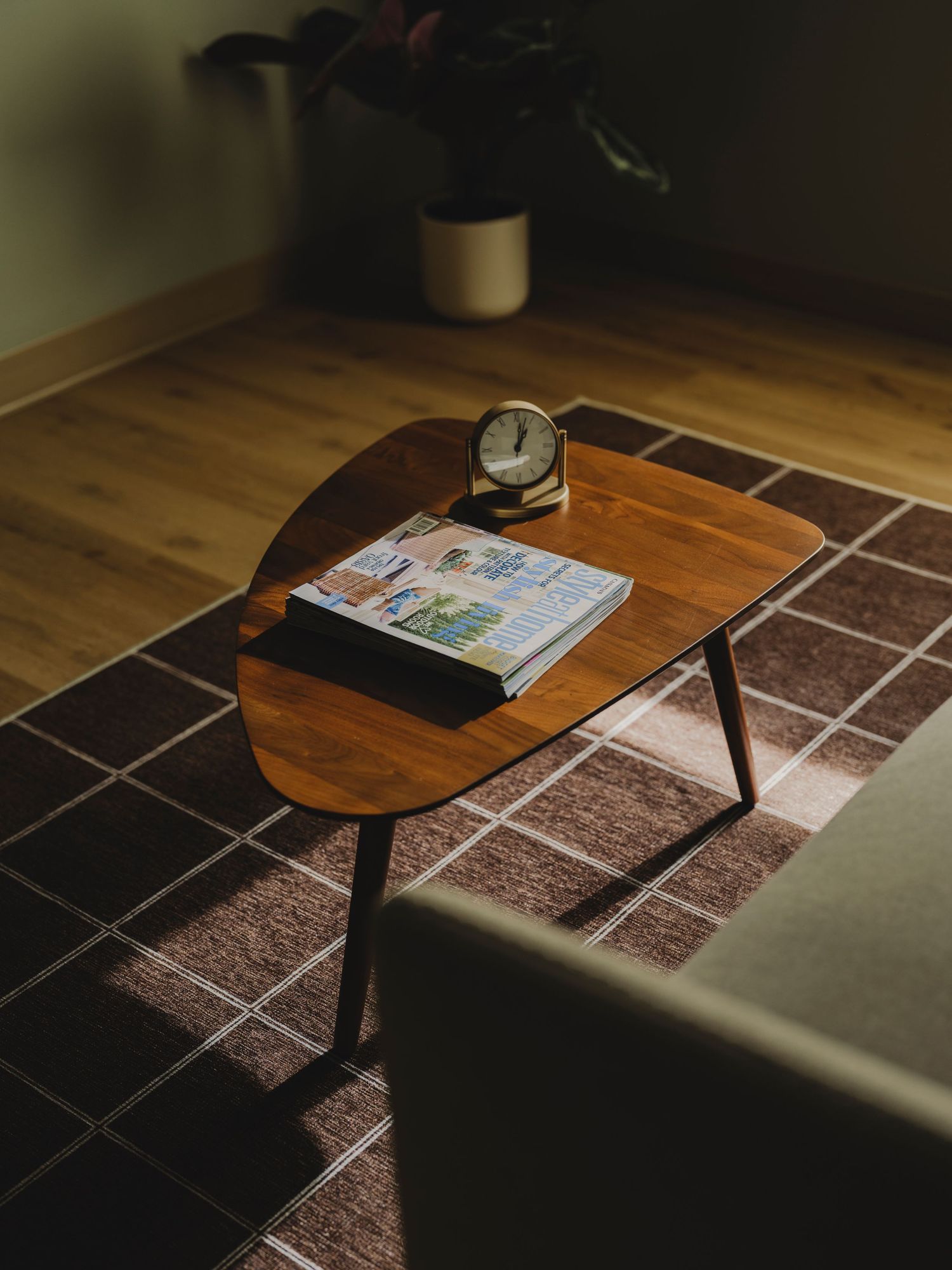Warm-toned coffee table with clock and magazine on plaid rug in softly lit mid-century modern room.