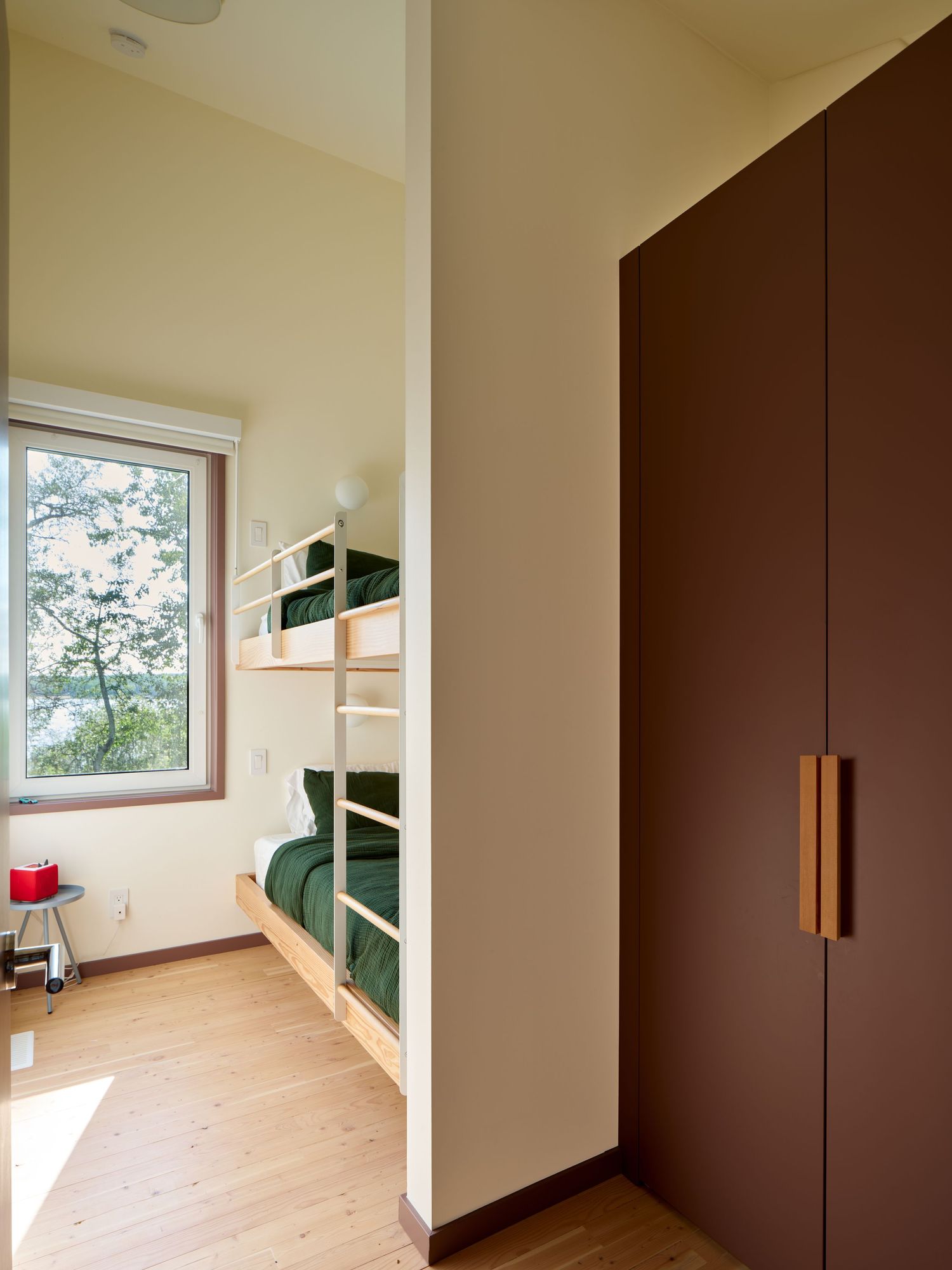 Modern kids room with built-in bunk beds, dark brown wardrobe, light wood floors, and green bedding.