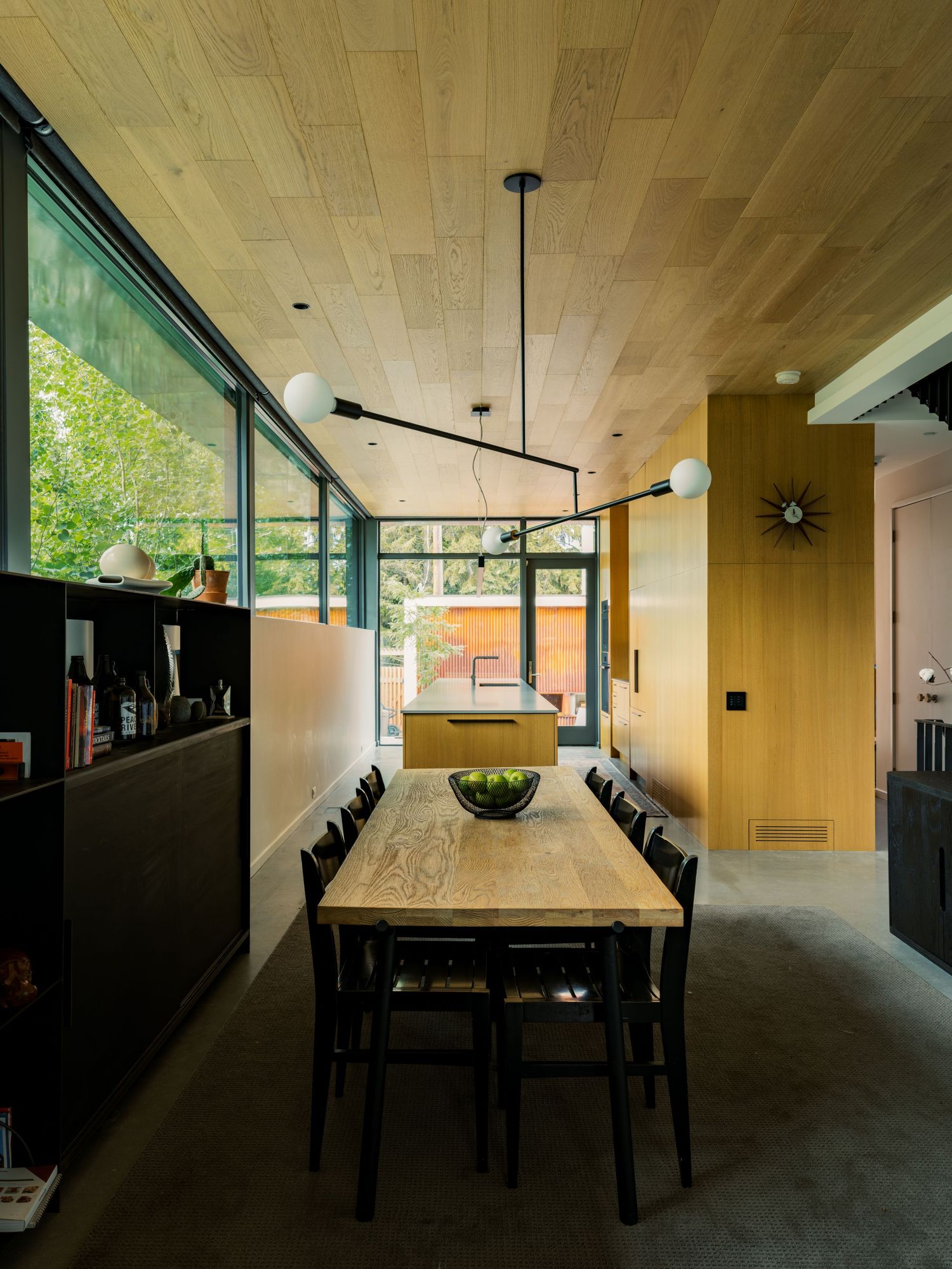 Modern dining room with wood ceiling, black pendant light, long wood table, black chairs, and floor-to-ceiling windows.