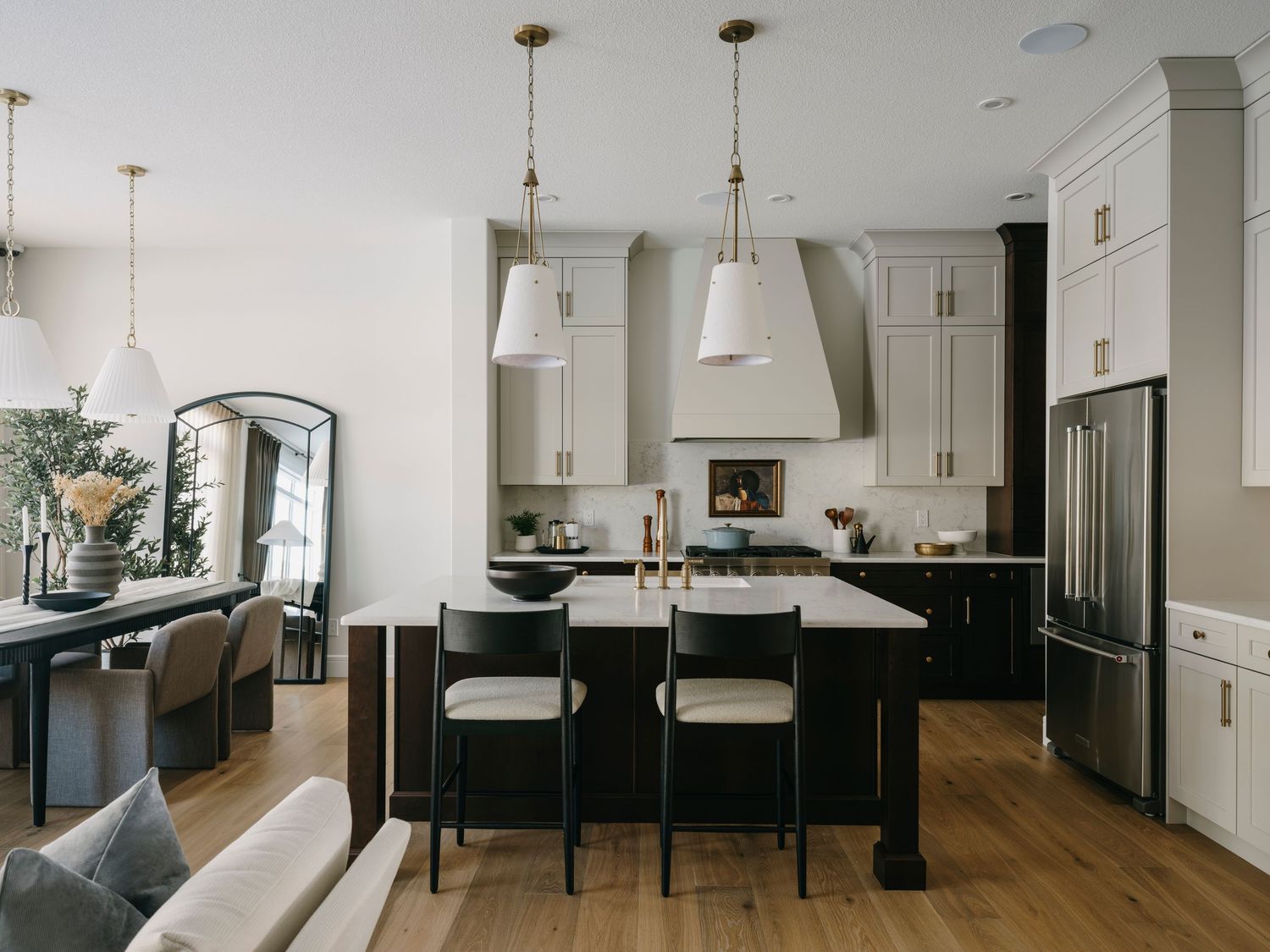 Open-concept kitchen with dark island, white cabinetry, pendant lights, and bar stools on hardwood floors.