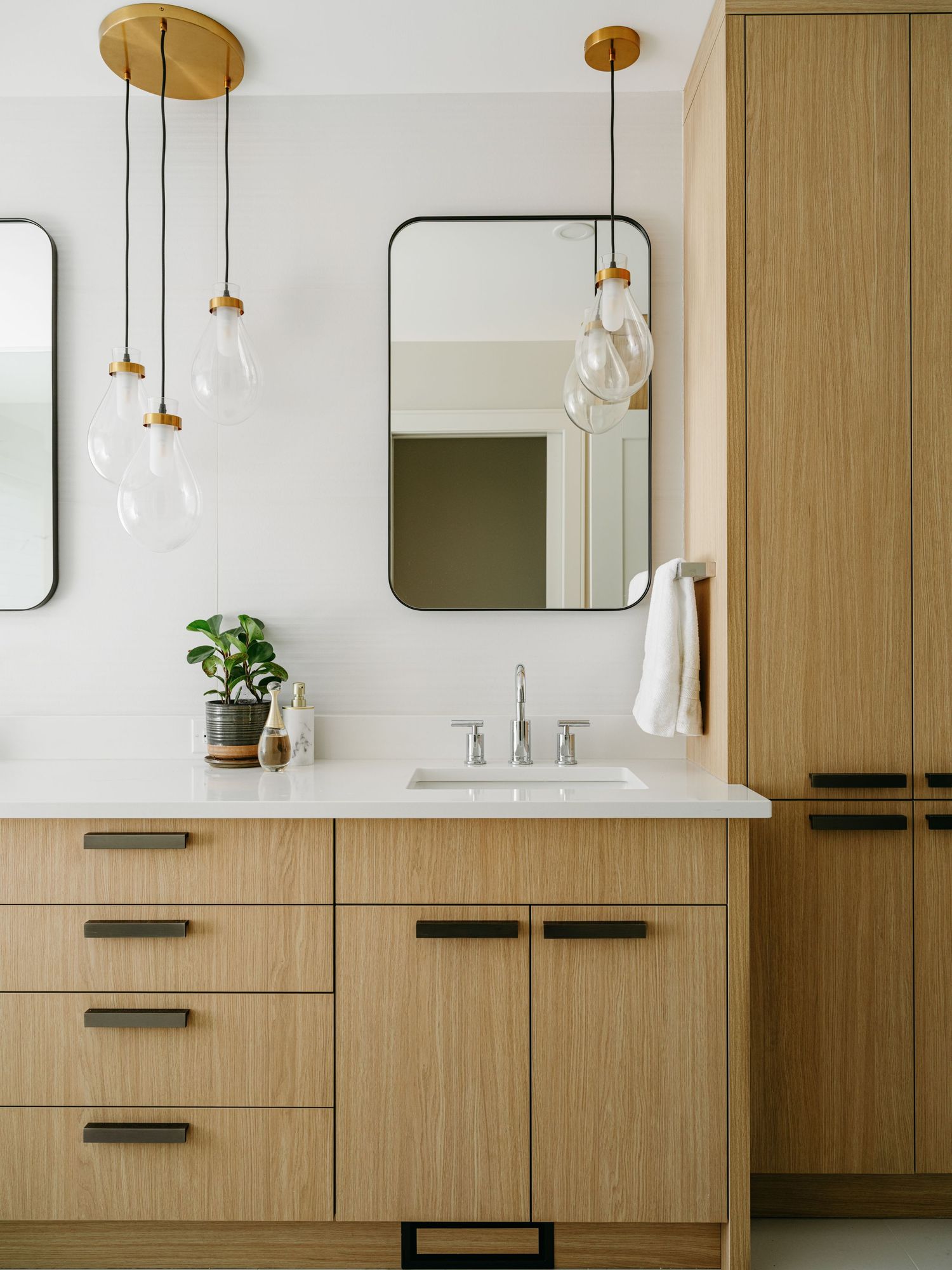 Contemporary bathroom with light oak wood vanity, black drawer pulls, glass pendant lights, and white quartz countertop.