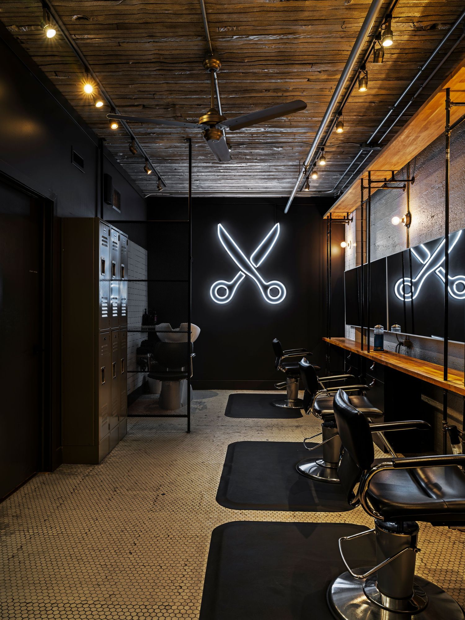 Industrial barbershop with neon scissors sign, barber chairs, wood ceiling, and track lighting.