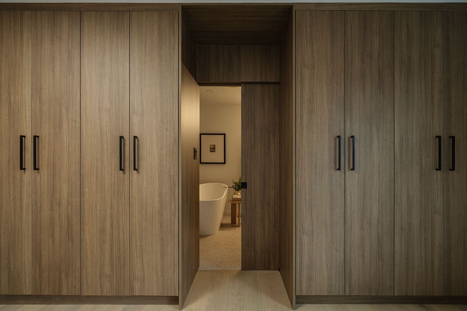Floor-to-ceiling wood grain wardrobe with black handles flanking a doorway leading to a bathroom.
