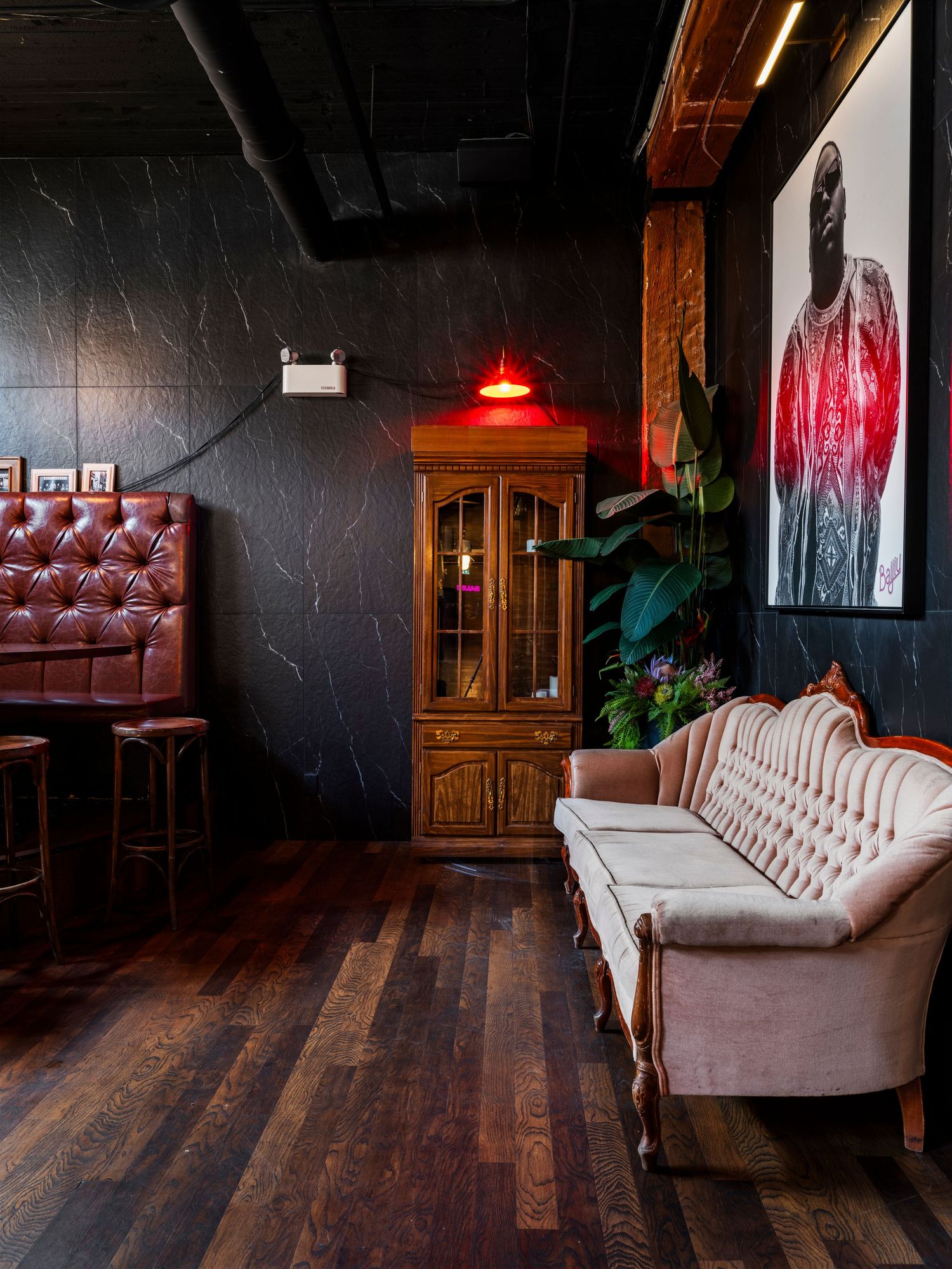Moody bar lounge with dark walls, vintage white sofa, tufted leather booth, and wooden cabinet.