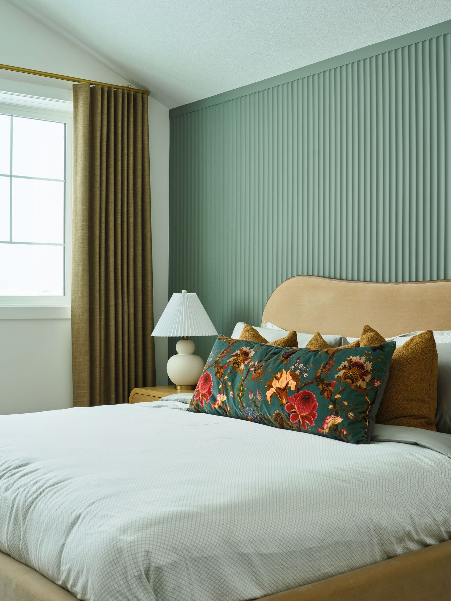Sage green fluted accent wall bedroom with camel velvet headboard, floral lumbar pillow, and olive curtains.