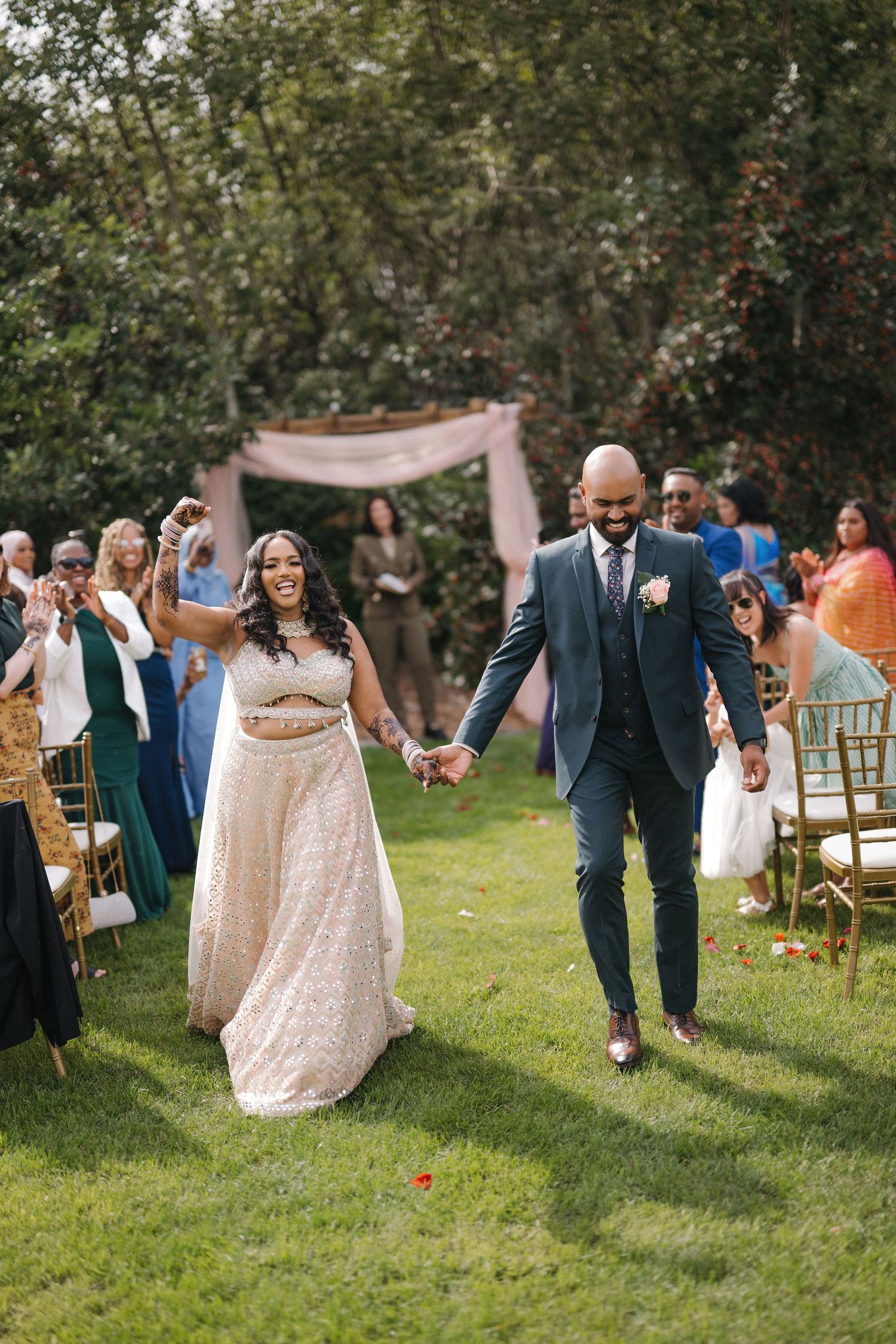 Joyful newlywed couple walking down outdoor ceremony aisle after wedding ceremony.