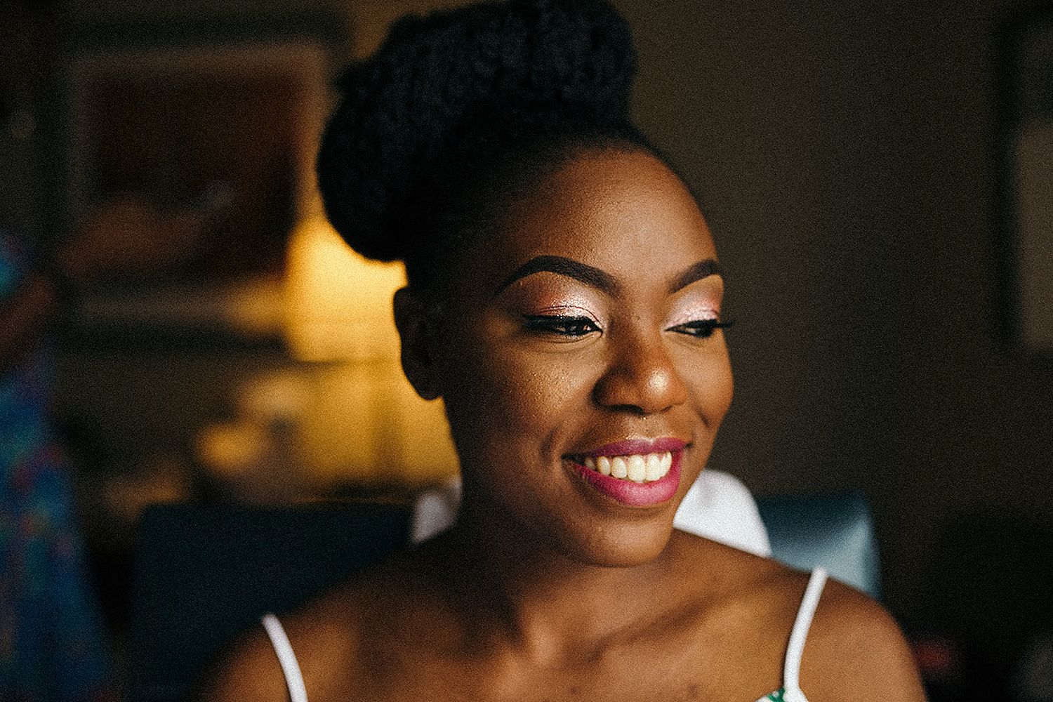 Close-up portrait of smiling Black woman with updo hairstyle and elegant makeup in warm lighting.
