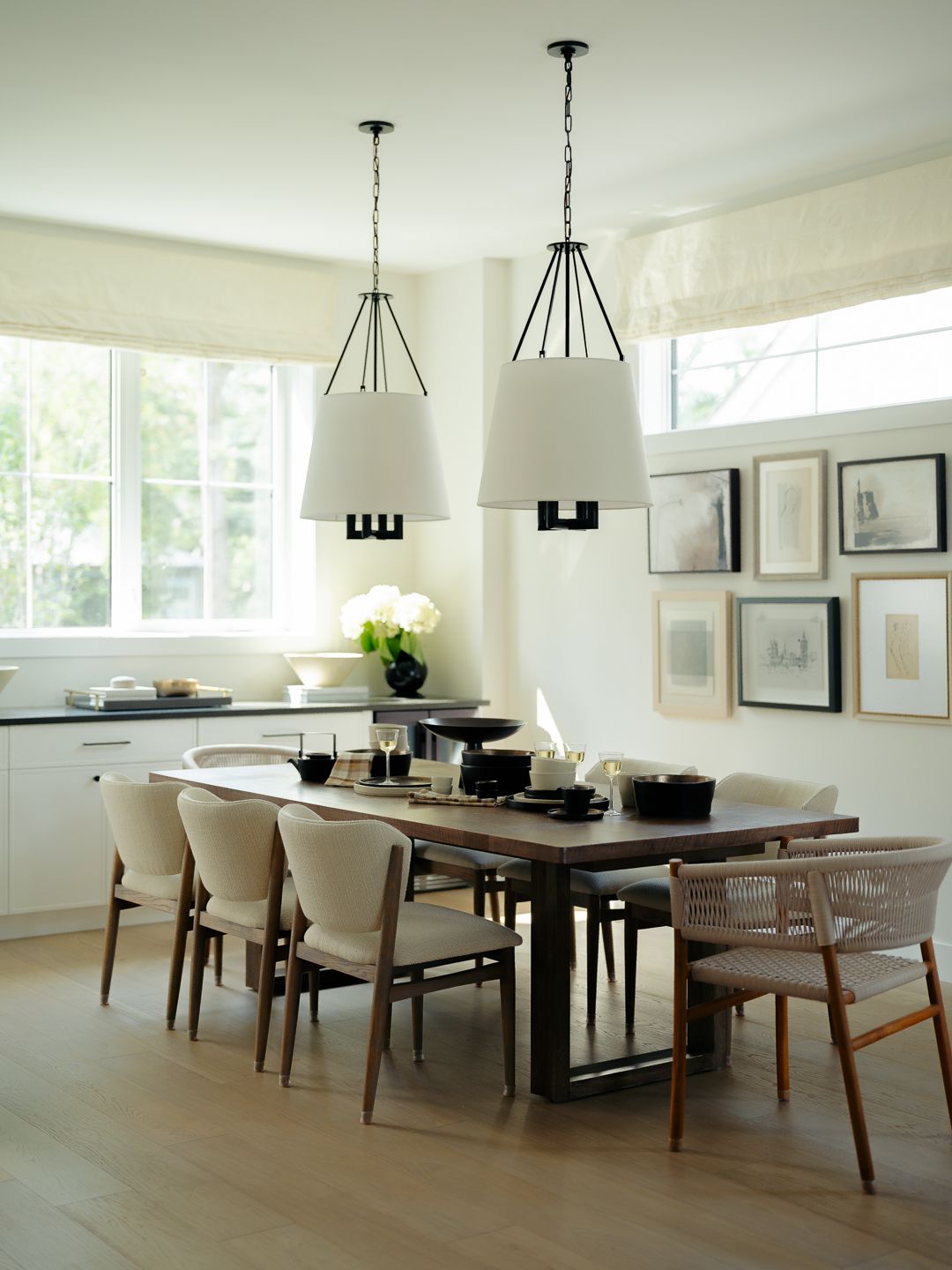 Bright dining room with dark wood table, cream chairs, pendant lights, gallery wall, and light hardwood floors.