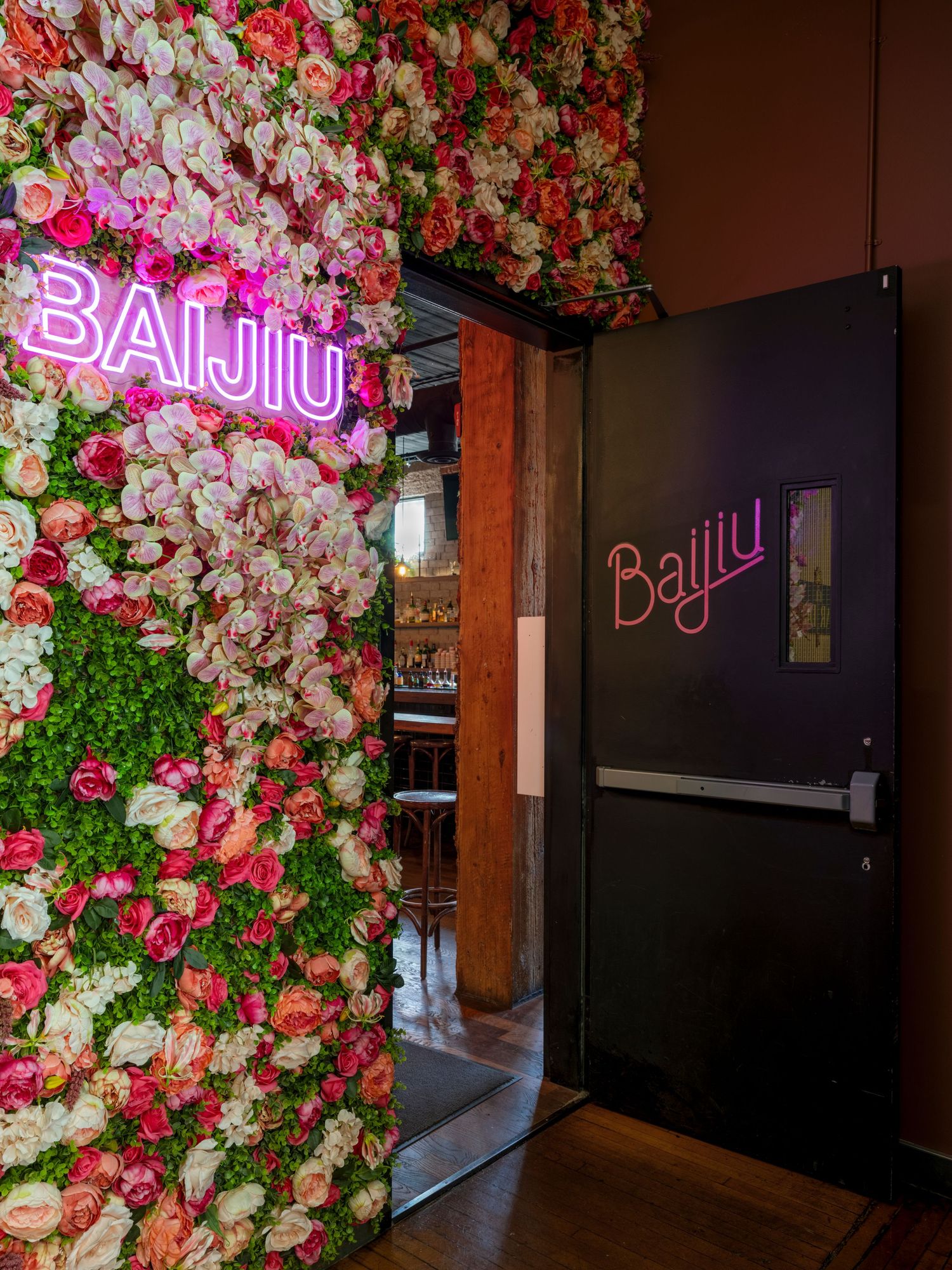 Baijiu restaurant entrance featuring a vibrant floral wall with pink neon sign and dark door.