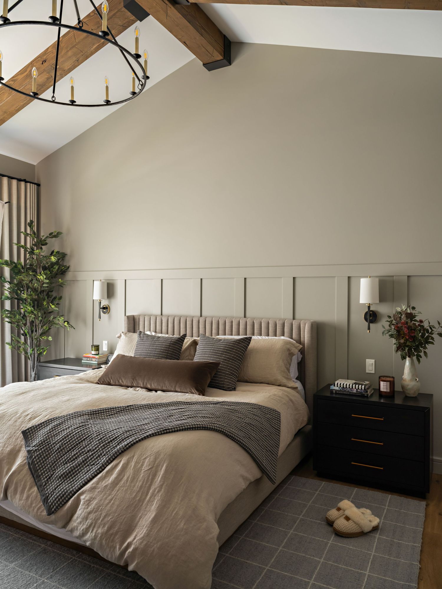 Elegant bedroom with vaulted ceiling, exposed wood beams, chandelier, tufted headboard, and sage wainscoting.