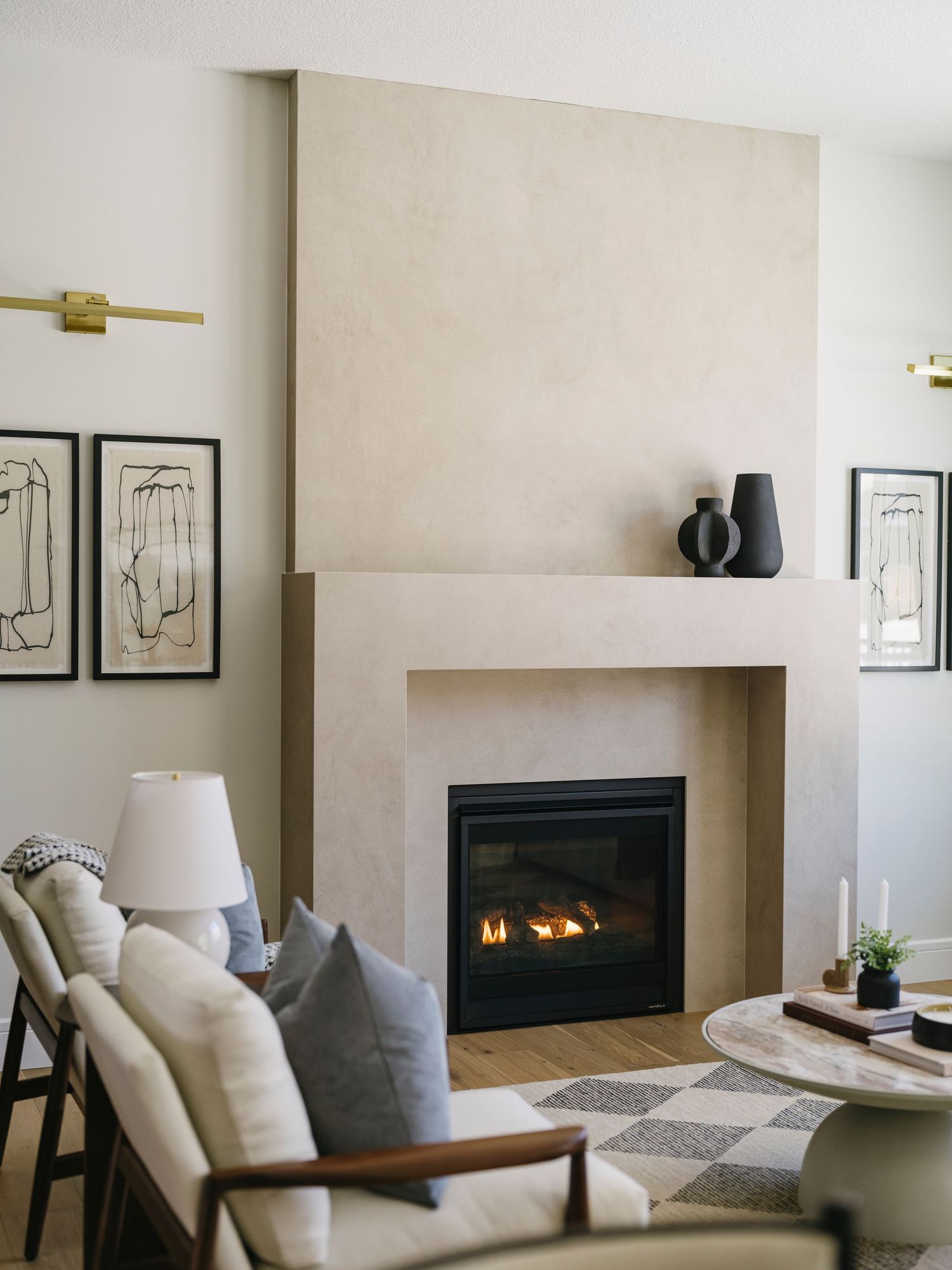 Minimalist living room with plaster fireplace surround, modern furniture, blue pillows, and abstract wall art.
