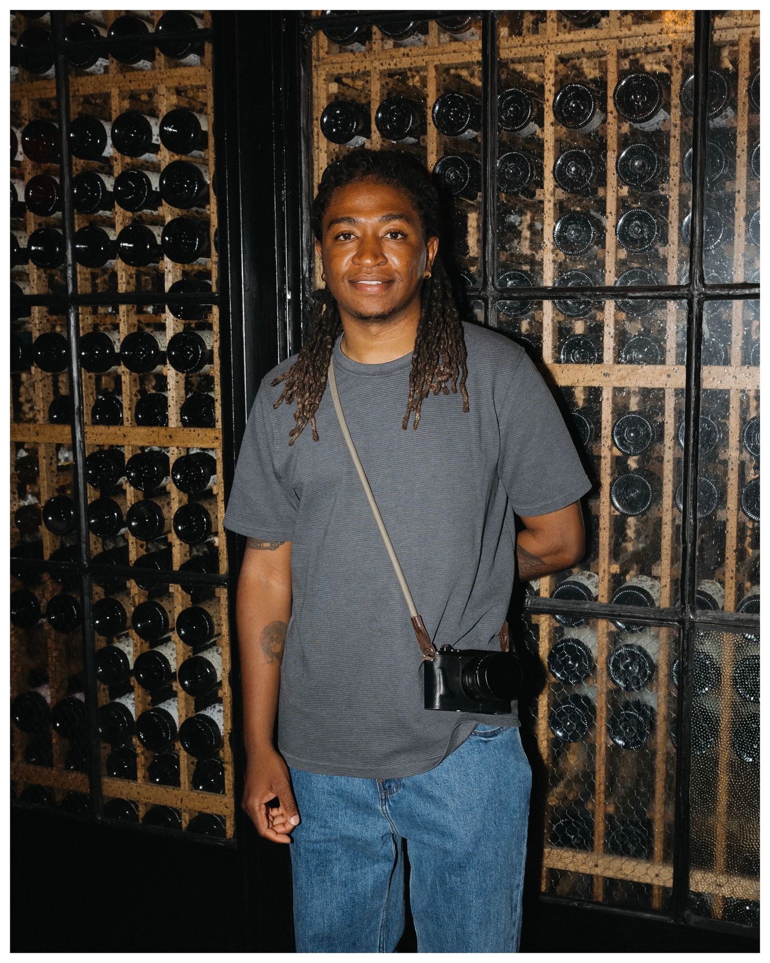 Edmonton-based photographer Ayo Erinle standing in front of a wine cellar — portrait of the photographer behind Ayoerinle.co.