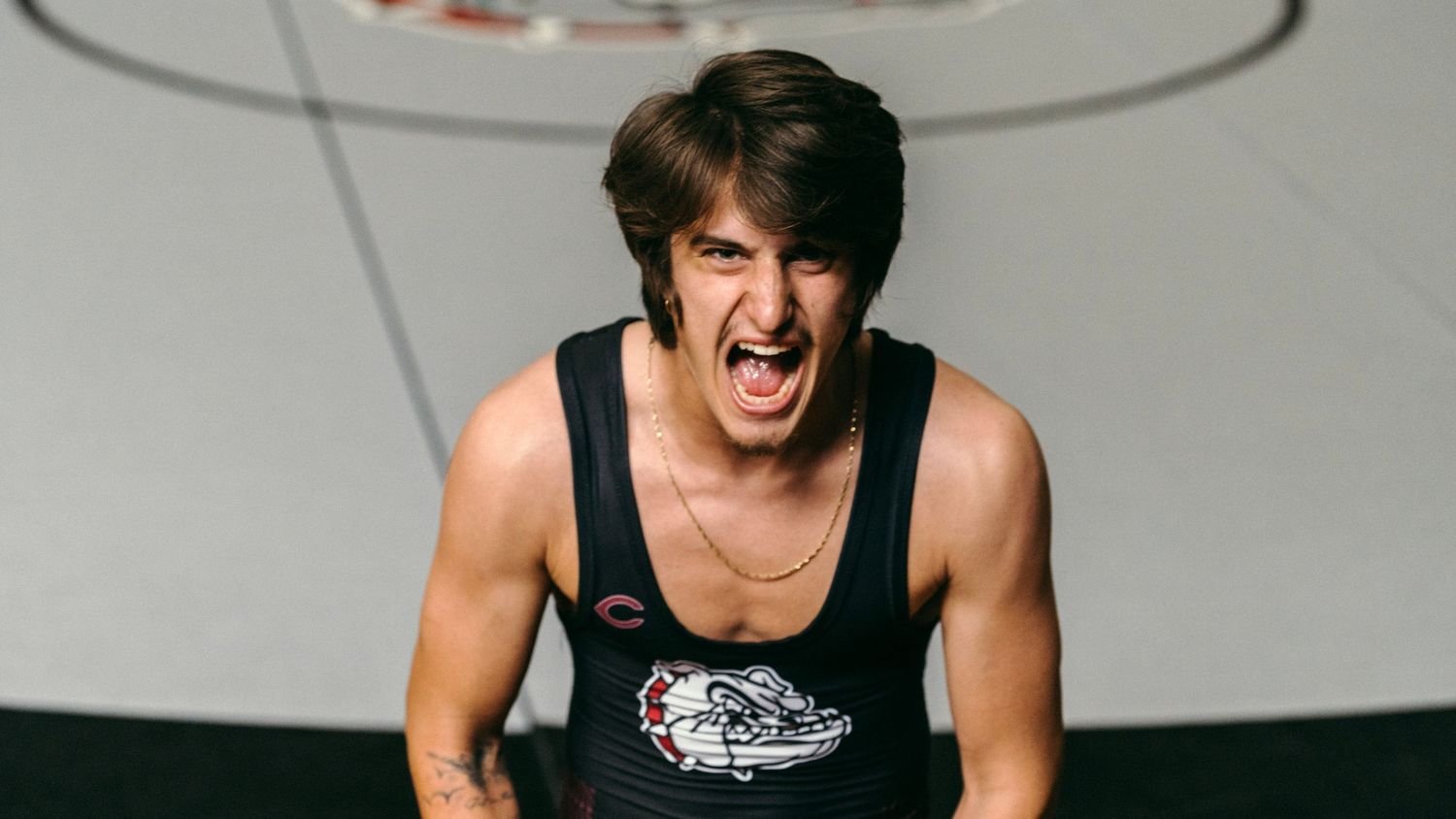 Young man in a wrestling tank top posing aggressively in a gym setting.