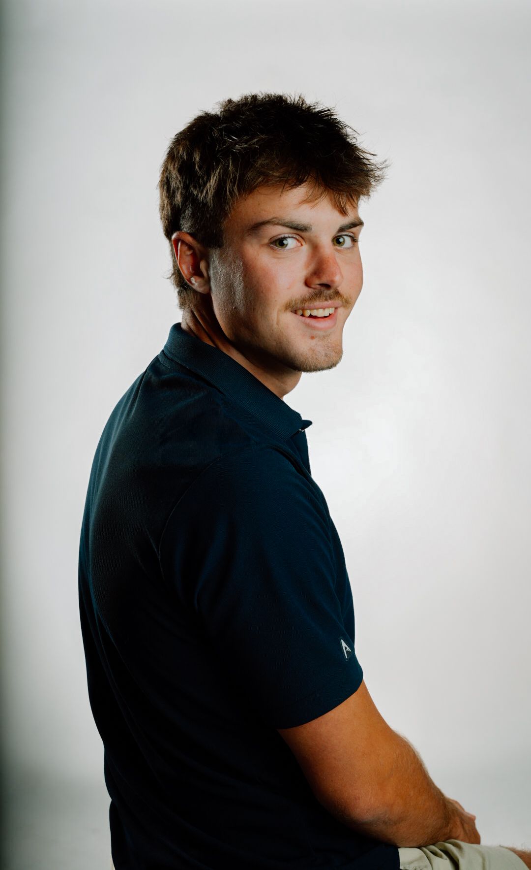 Young man in navy polo shirt smiling over shoulder in professional studio portrait photo.
