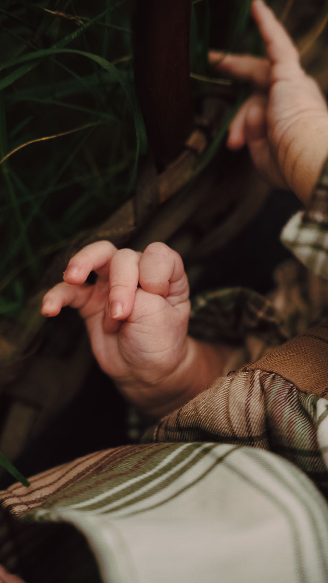 Close-up of a newborn baby's tiny hand with delicate fingers, resting on a soft plaid blanket outdoors.