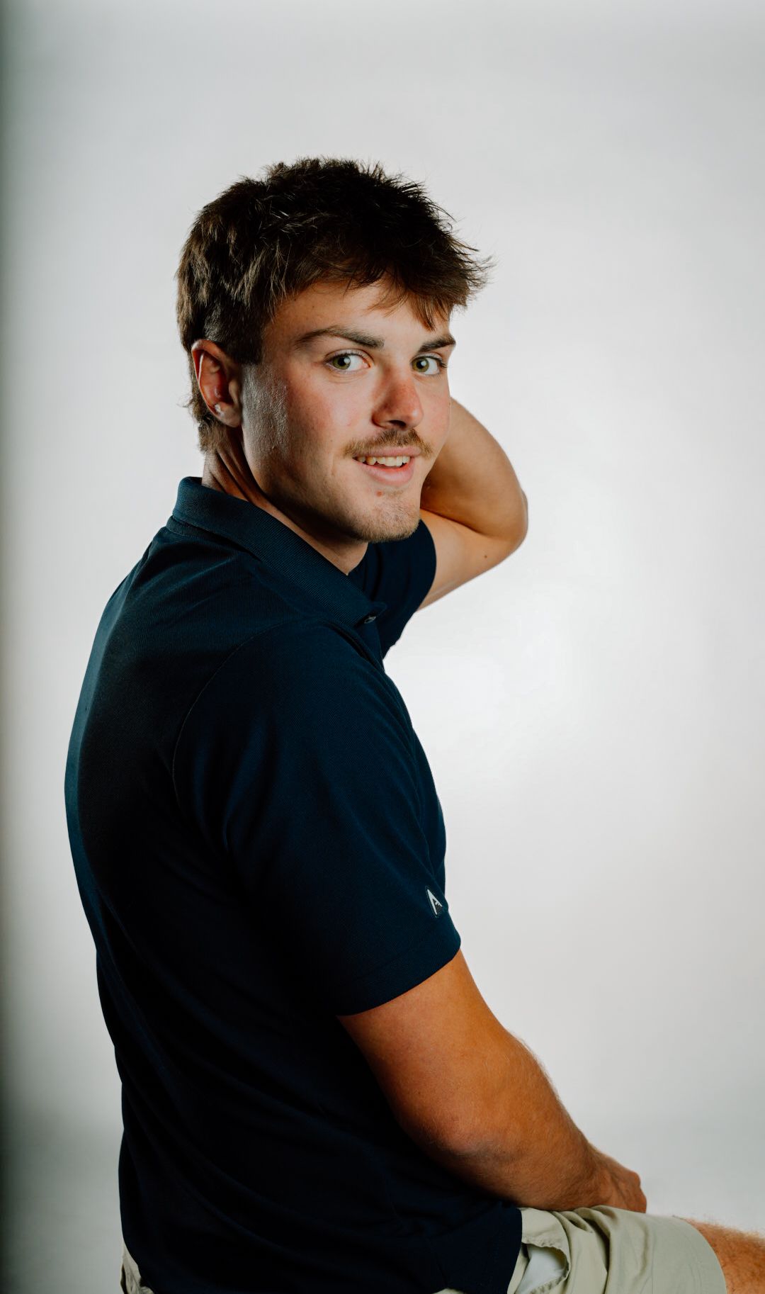 Young man in navy polo shirt posing confidently against white background in a professional portrait photo.