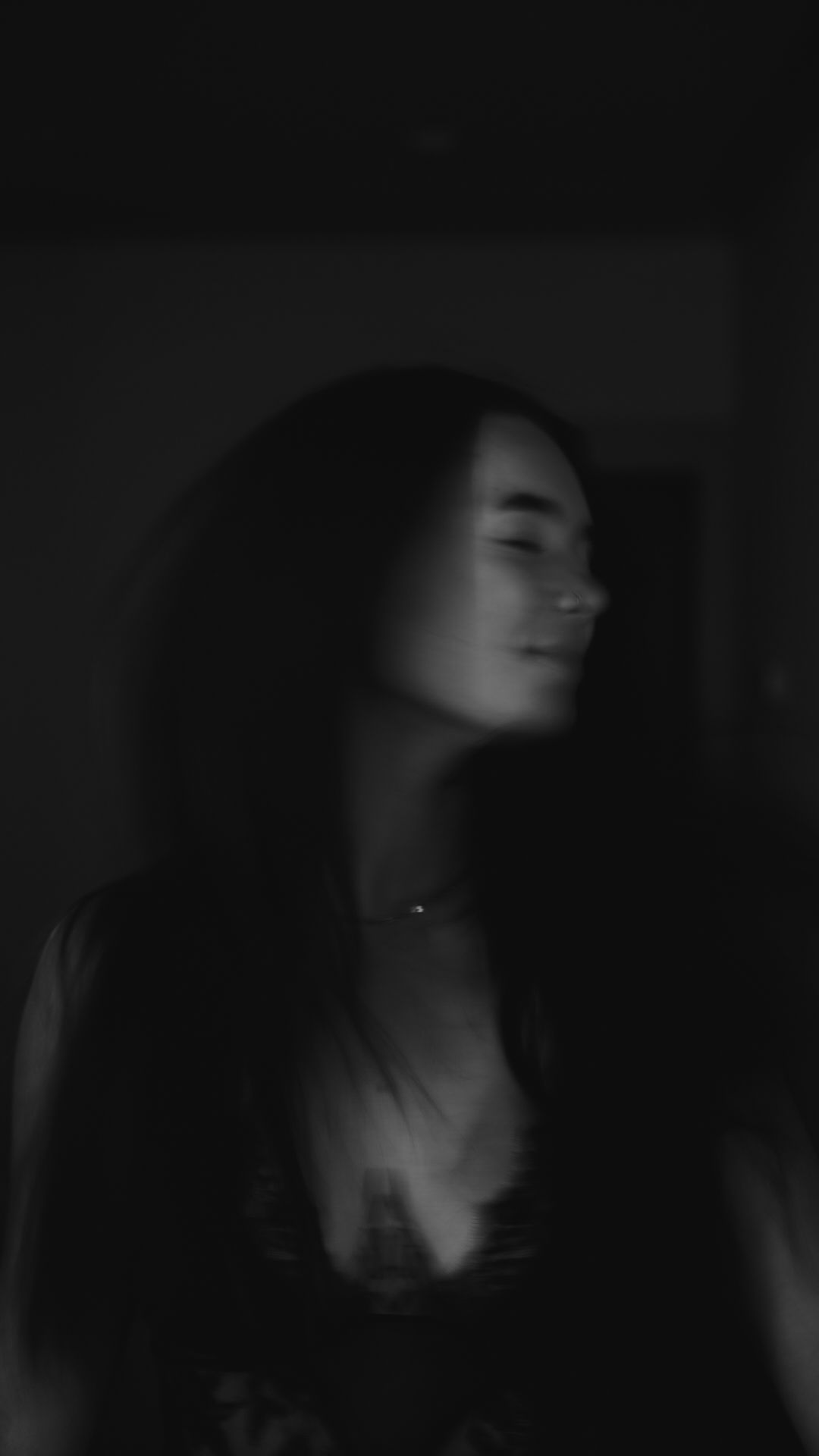 Black and white moody portrait of a young woman with long dark hair posing in dim lighting.