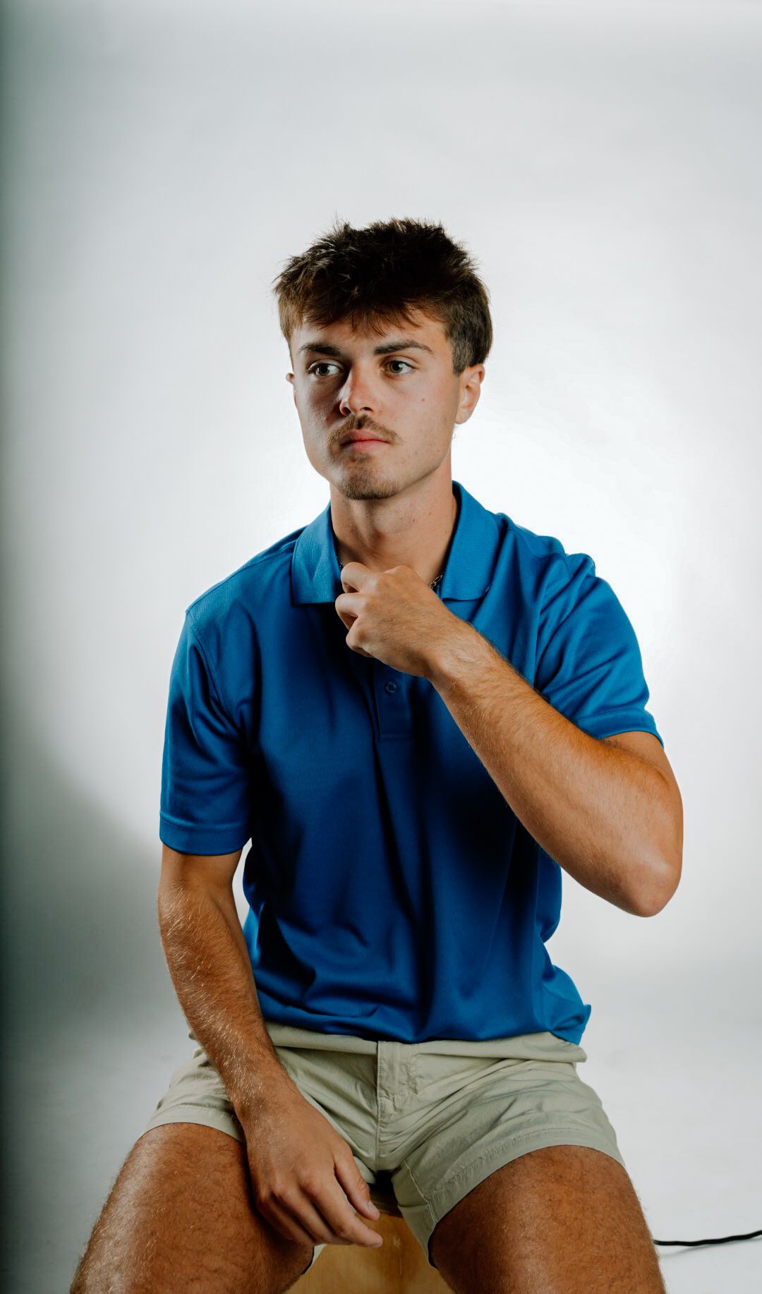 Young man in blue polo shirt sitting confidently against white background.