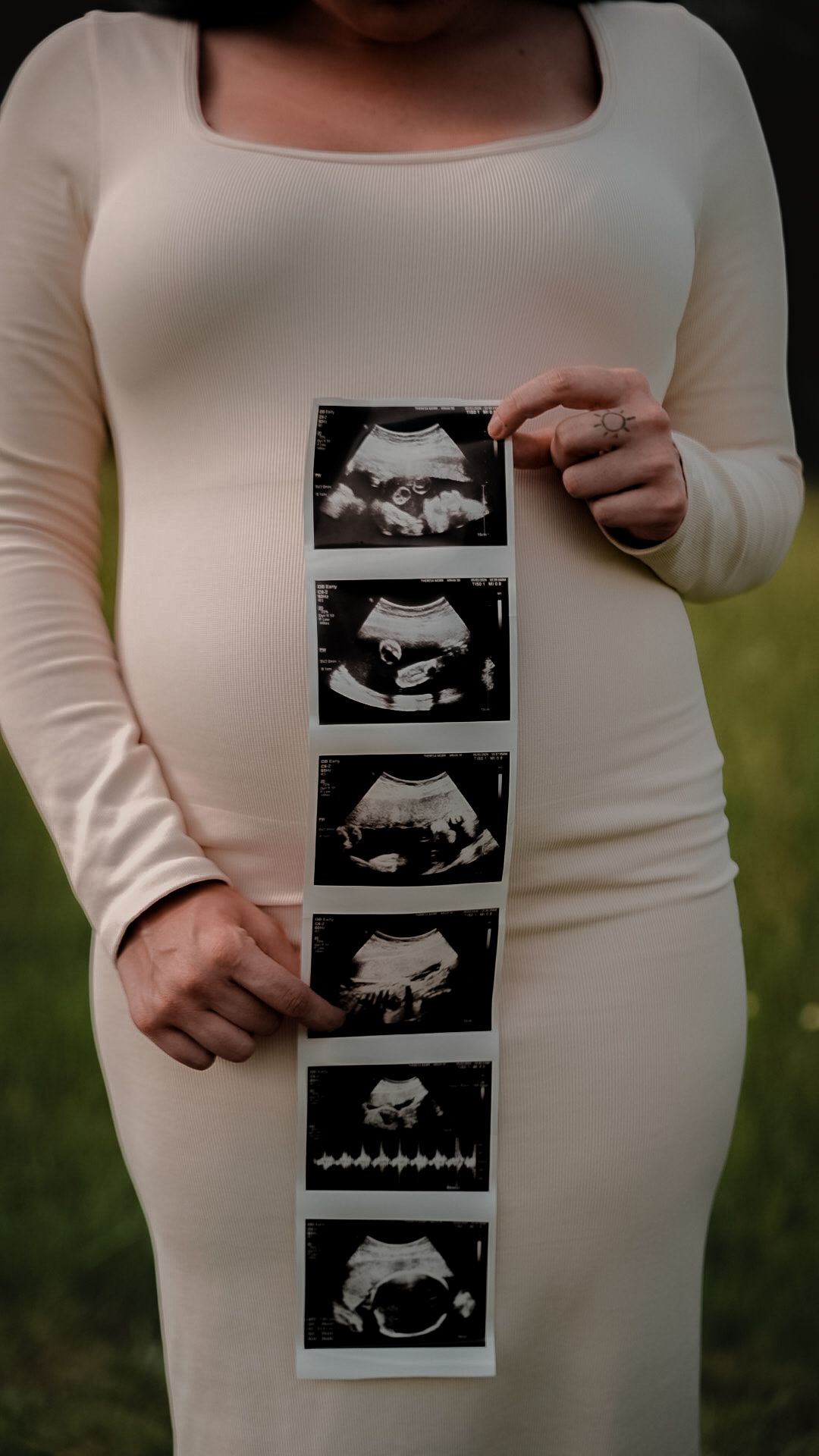 Pregnant woman in cream dress holding ultrasound photo strip showing baby development stages.