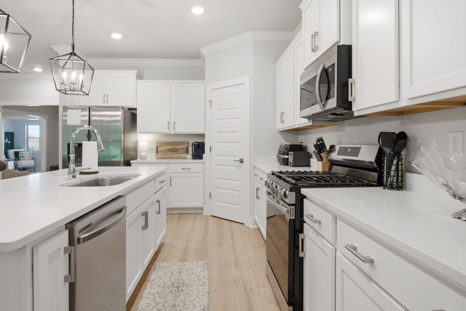 Modern white kitchen with stainless steel appliances, quartz countertops, pendant lighting, and light hardwood floors.
