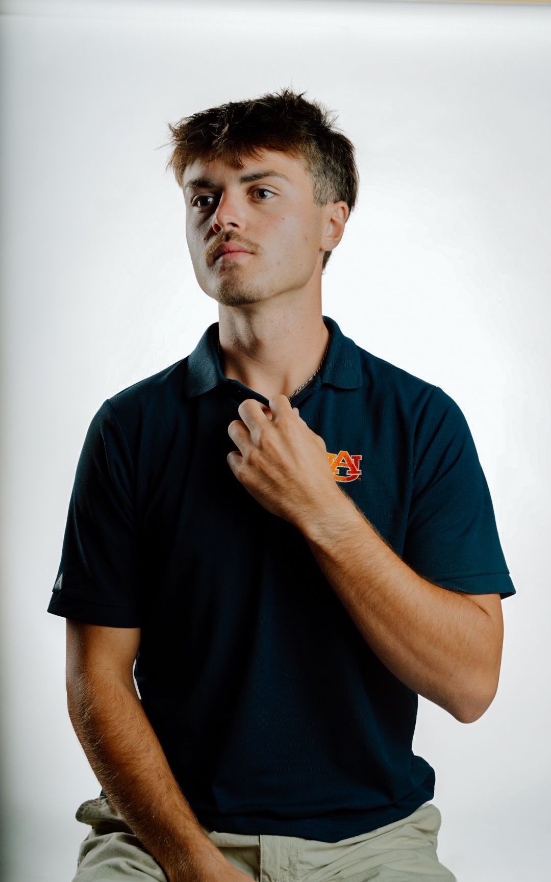 Young man in Auburn University navy polo shirt posing confidently against white background.