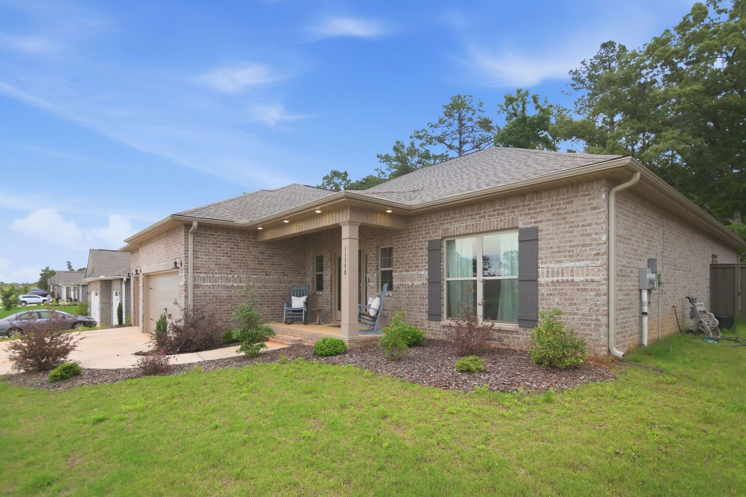 Brick ranch-style home with manicured lawn, shuttered windows, attached garage, and tall pine trees in background.