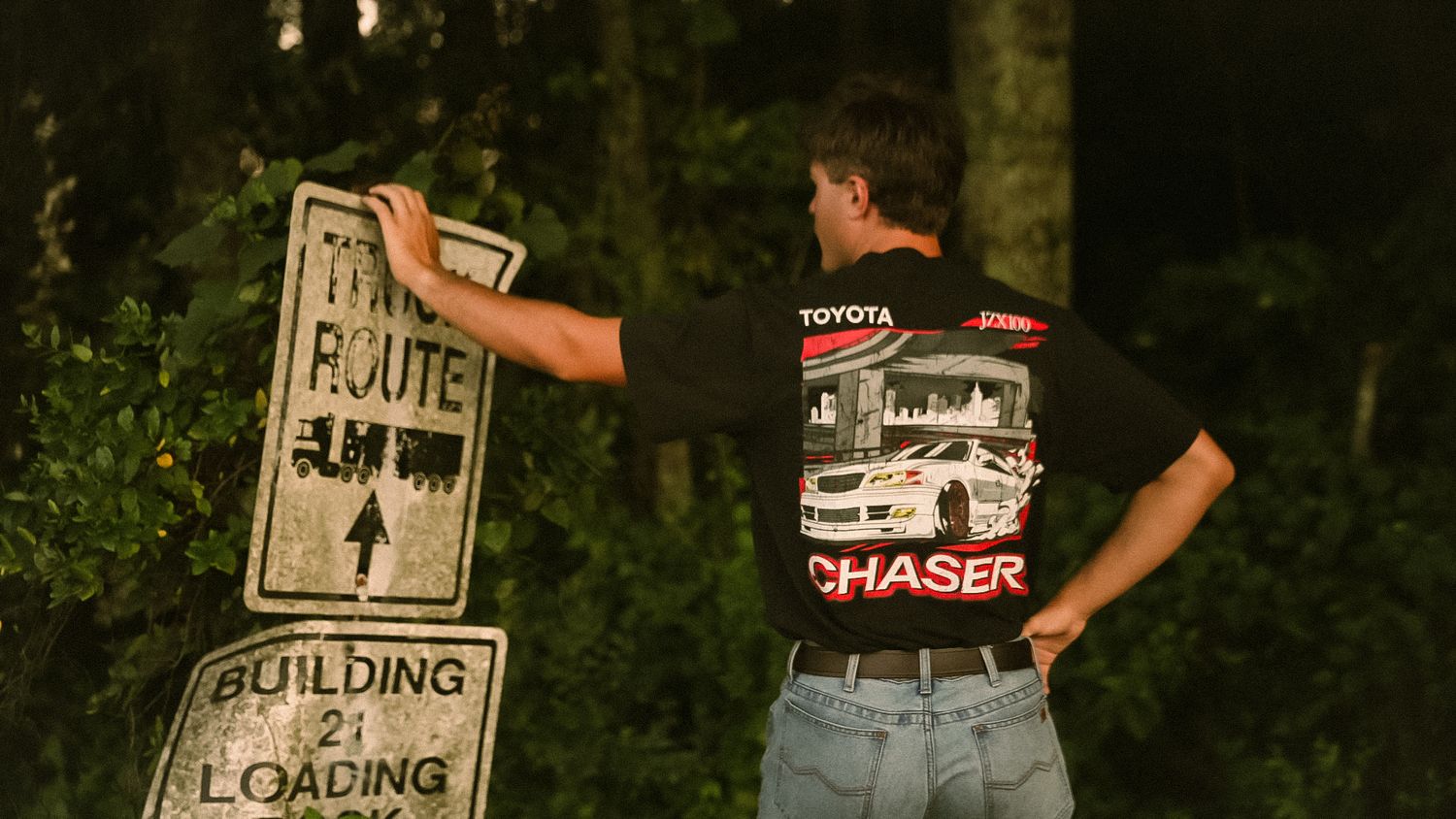 Man in Toyota Chaser t-shirt examines a Route sign near a Building 2 Loading sign outdoors.