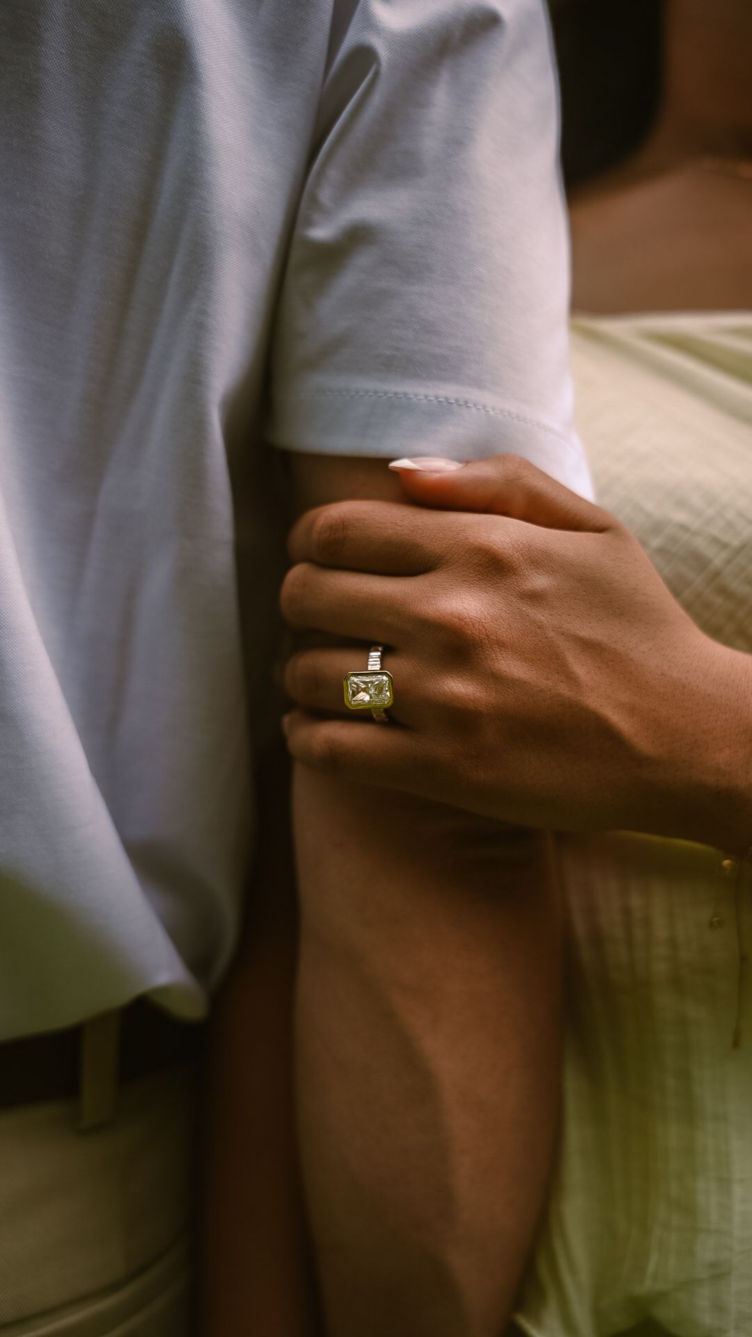 A hand with white nails wearing a yellow gemstone ring gently grips a person's arm in a close-up shot.