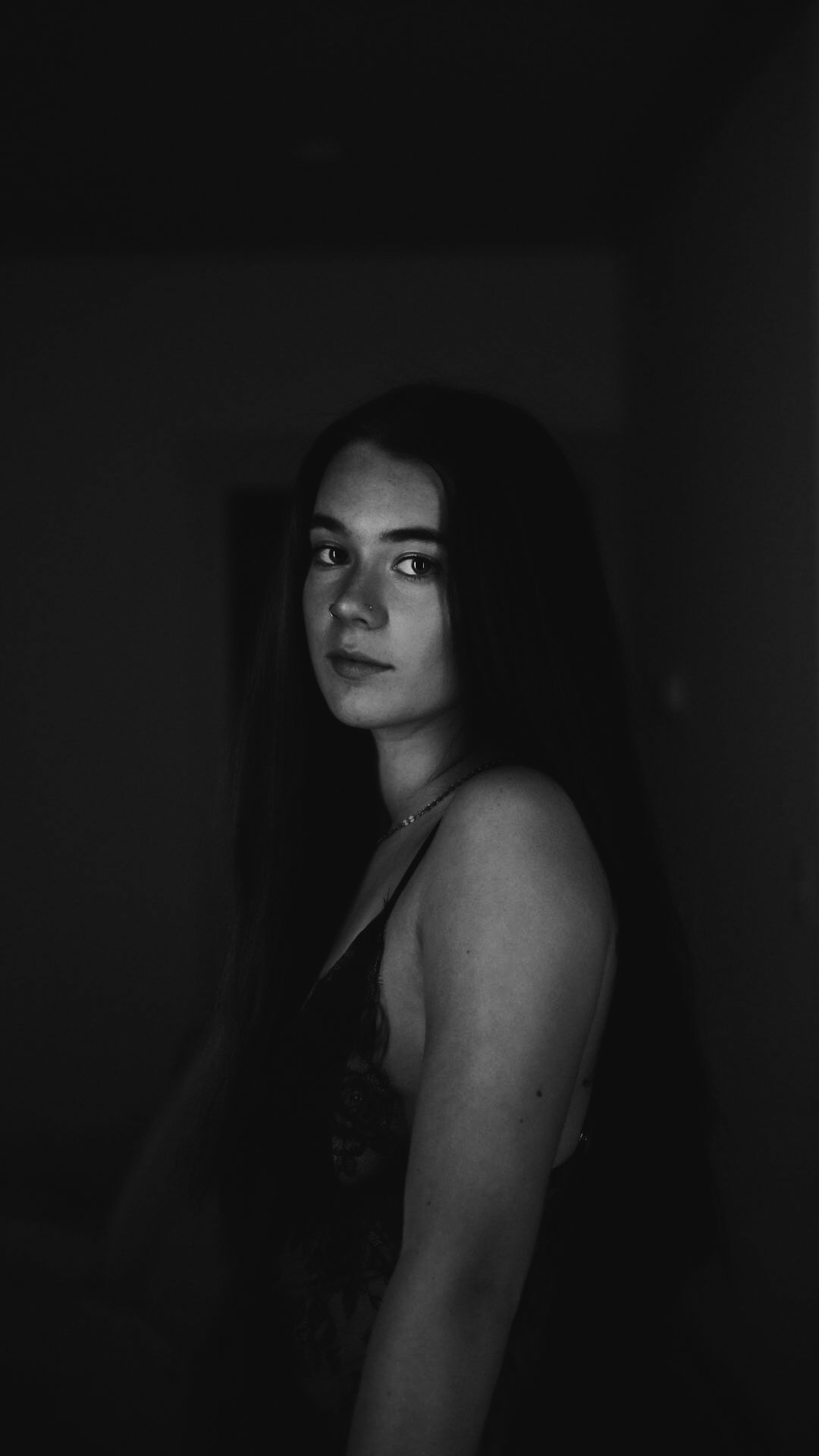 Black and white portrait of a young woman with long dark hair in a dimly lit room.
