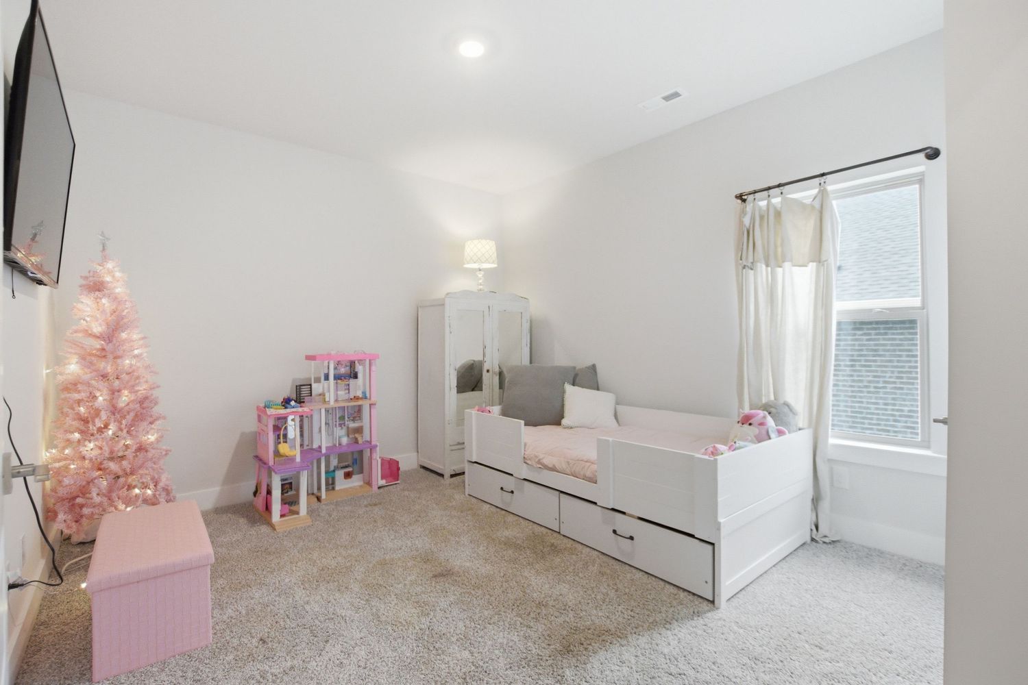 Bright girls bedroom with white daybed, pink Christmas tree, and dollhouse on carpet.