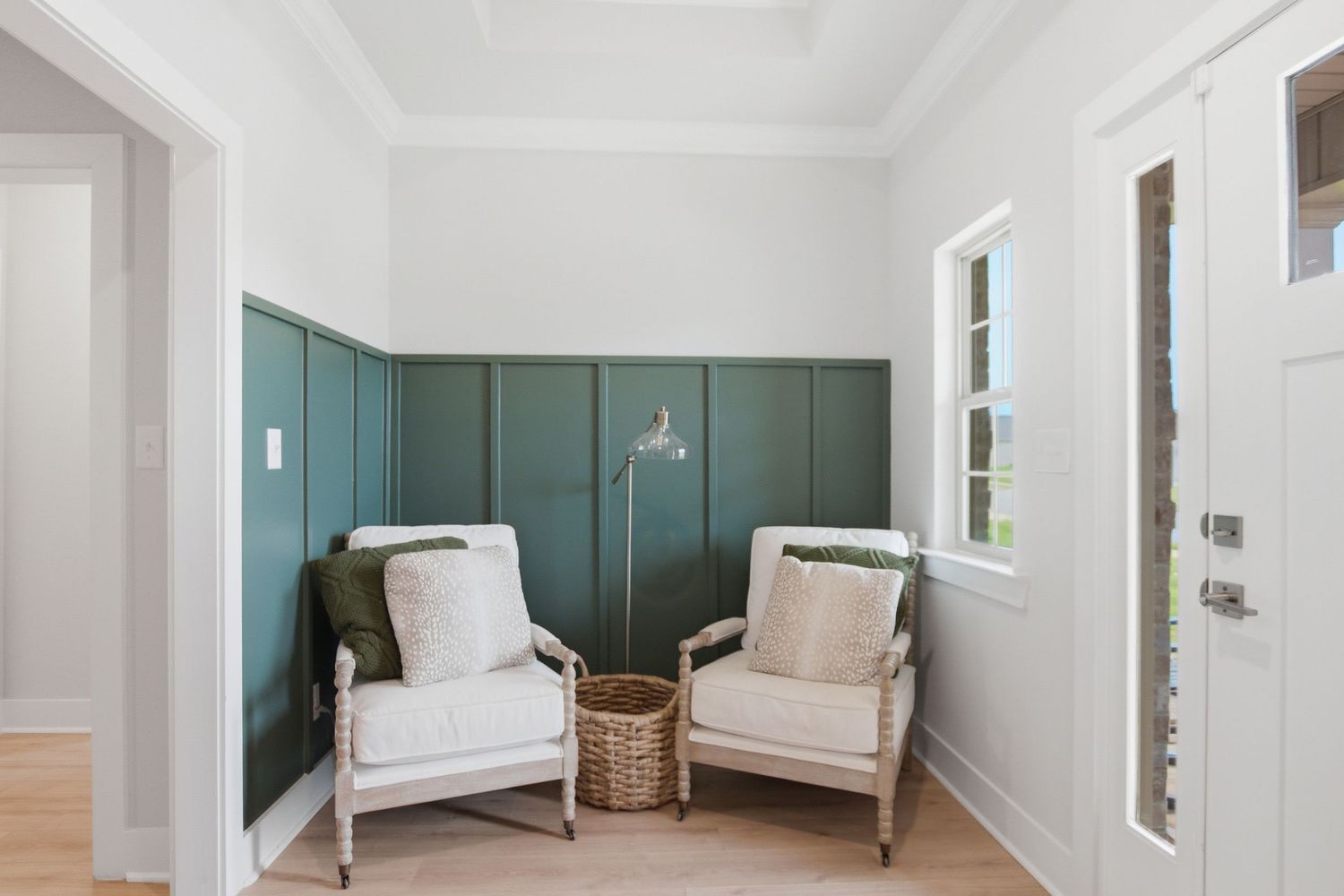 Elegant entryway with teal wainscoting, two white linen chairs, wicker basket, and natural light from a window.