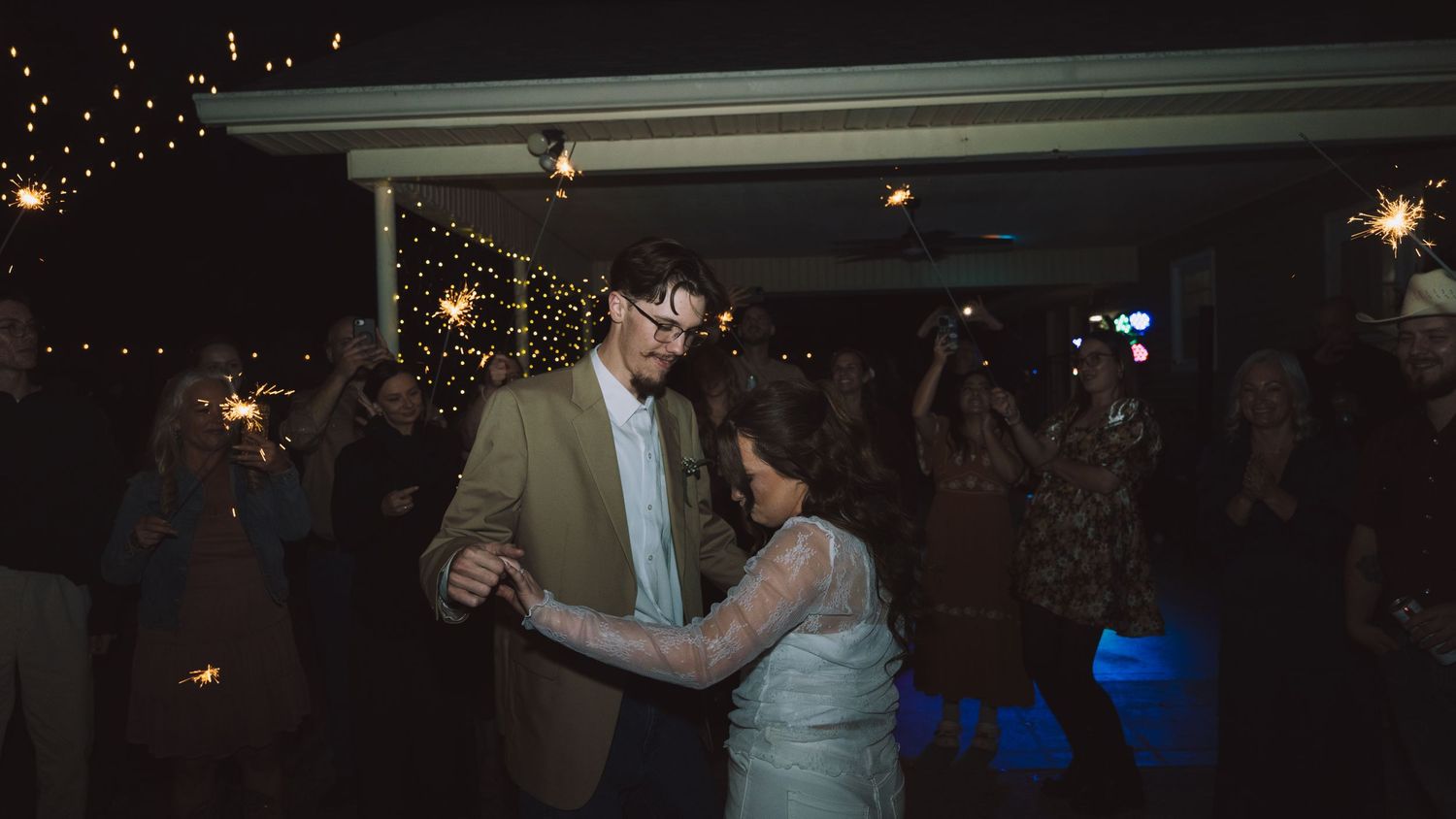 Couple shares first dance surrounded by guests holding sparklers at an outdoor evening wedding reception.
