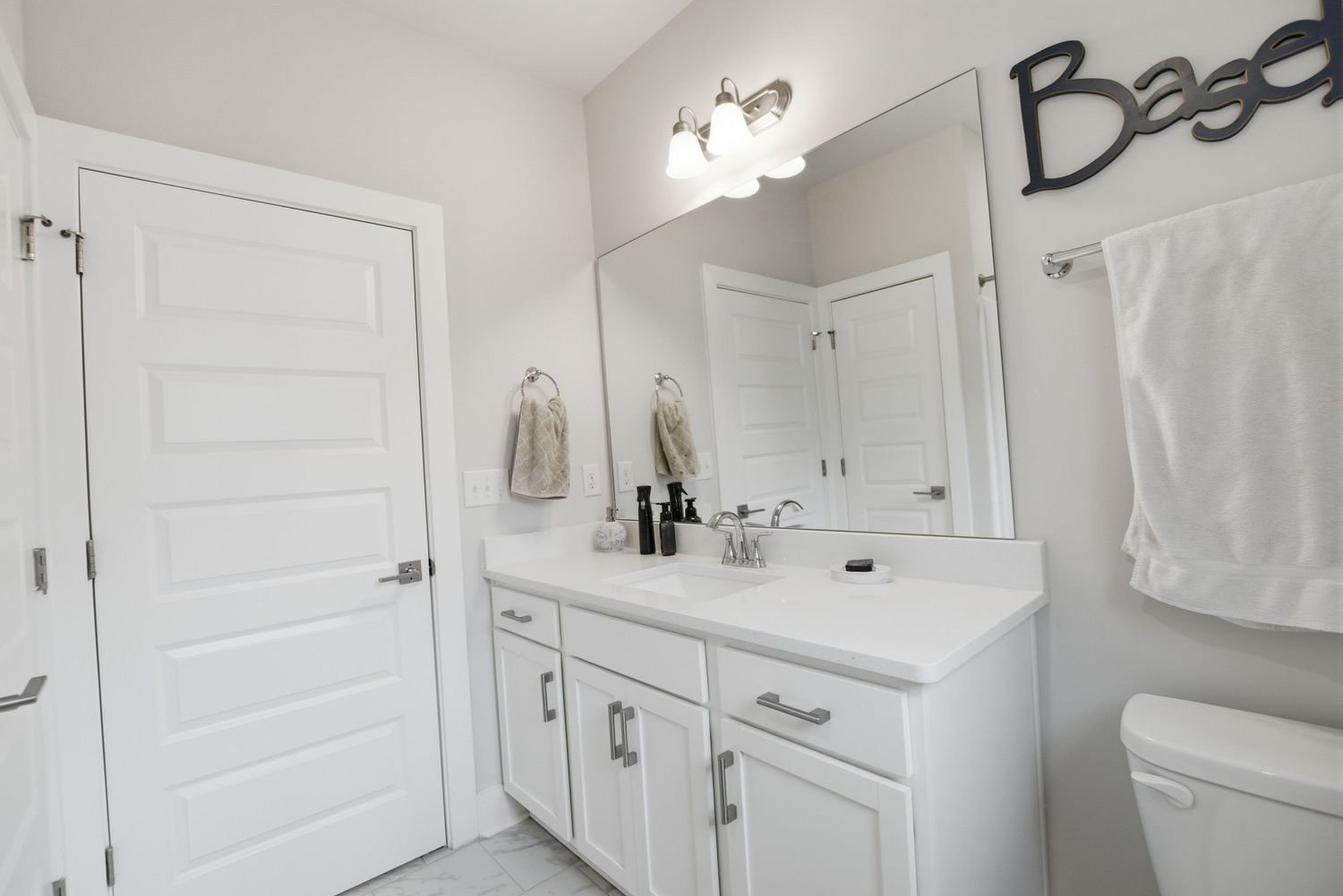 White bathroom vanity with single sink, large mirror, and decorative baseball sign on wall.