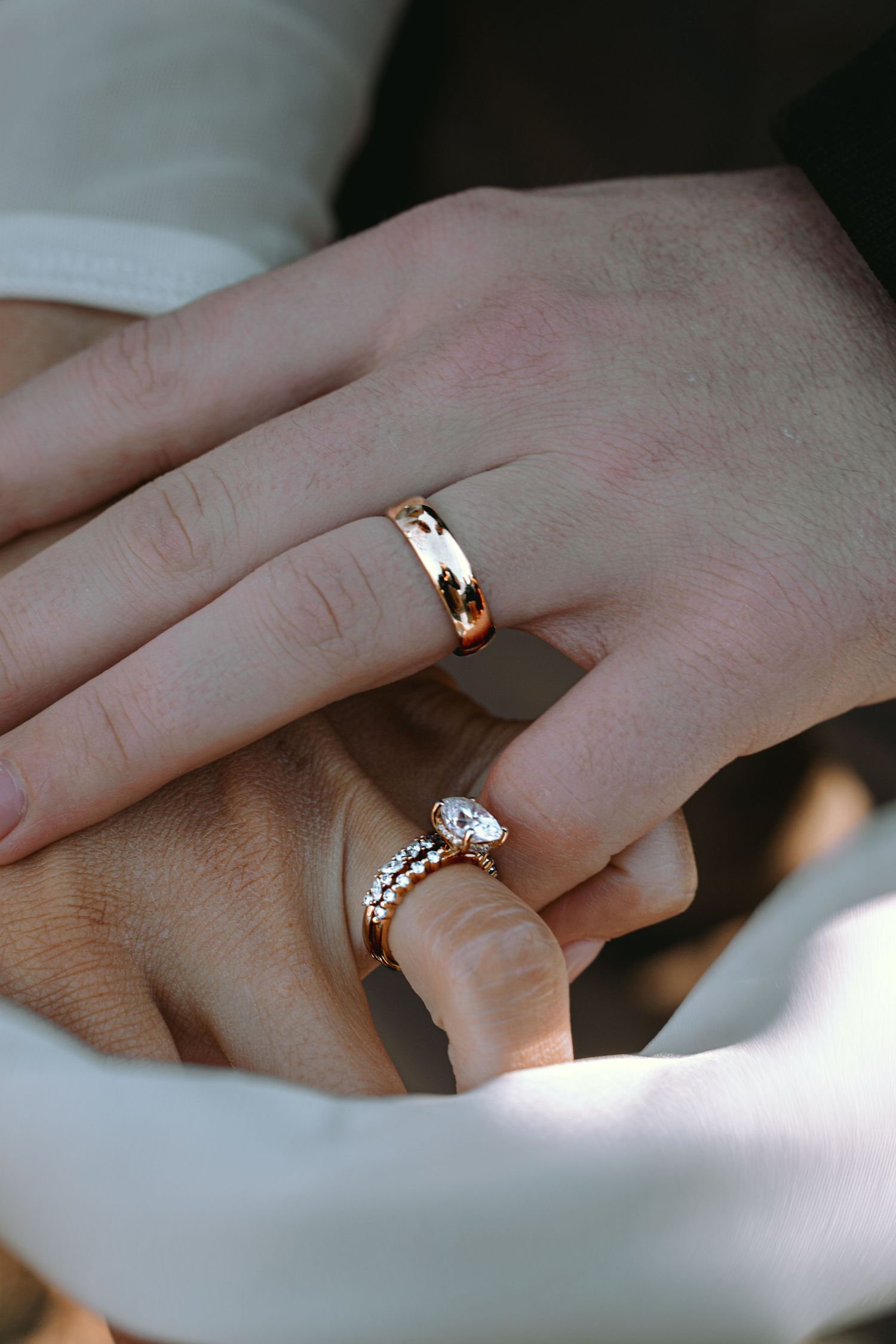 Close-up of couple holding hands wearing matching gold wedding and engagement rings.