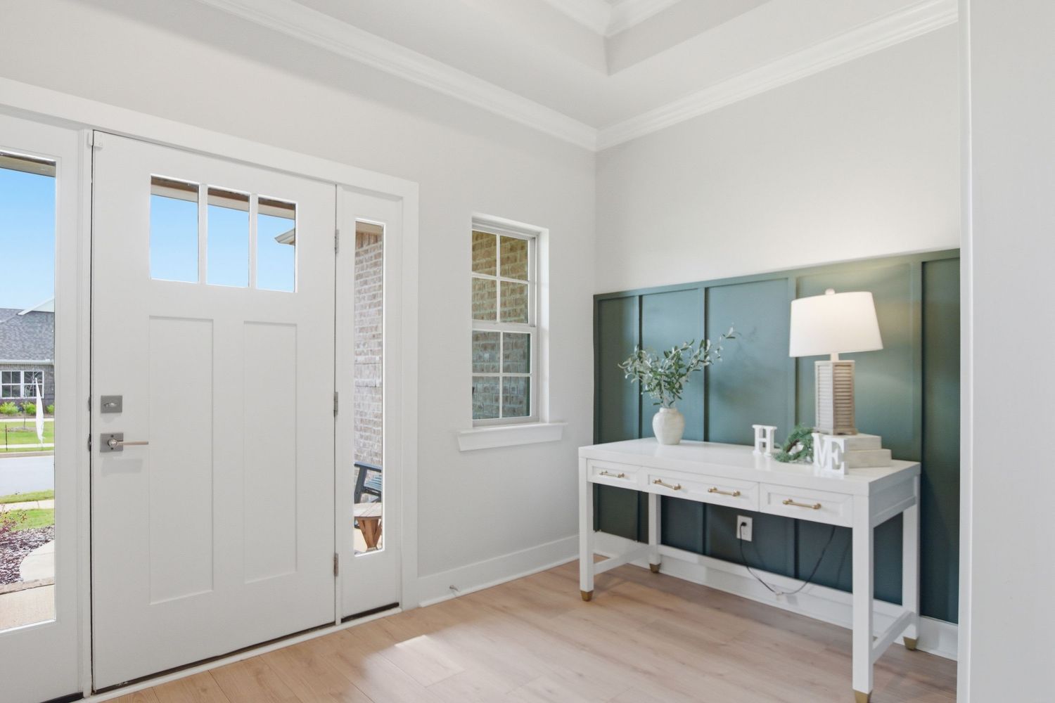 Bright entryway with white front door, hardwood floors, and elegant console table against teal wainscoting wall.