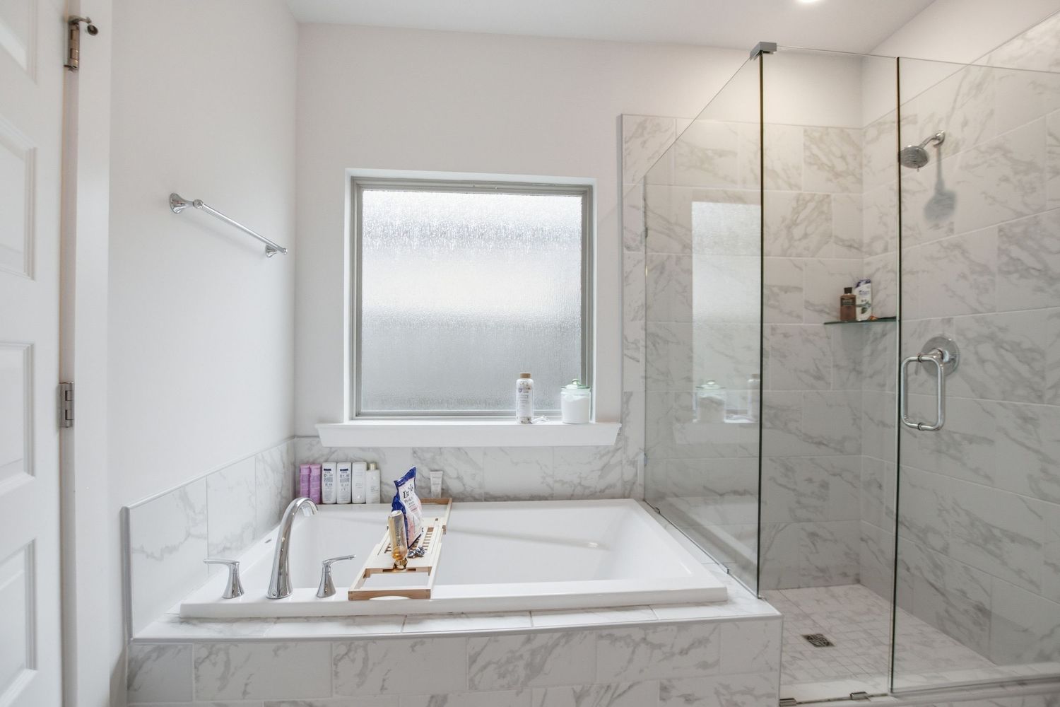 Luxurious master bathroom with marble soaking tub, glass shower enclosure, and marble tile walls.