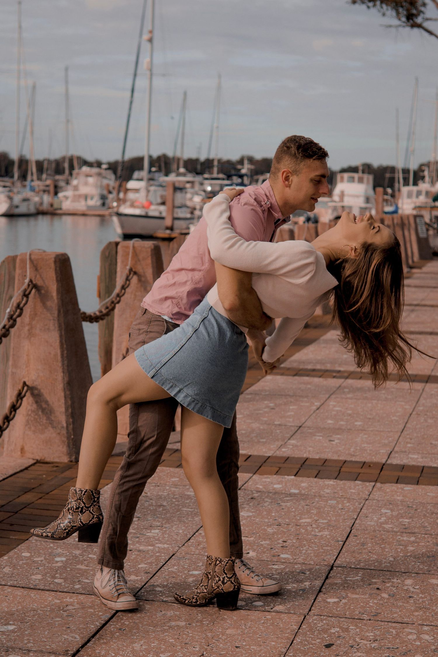Romantic couple sharing a dip kiss on a waterfront dock with sailboats in the background.
