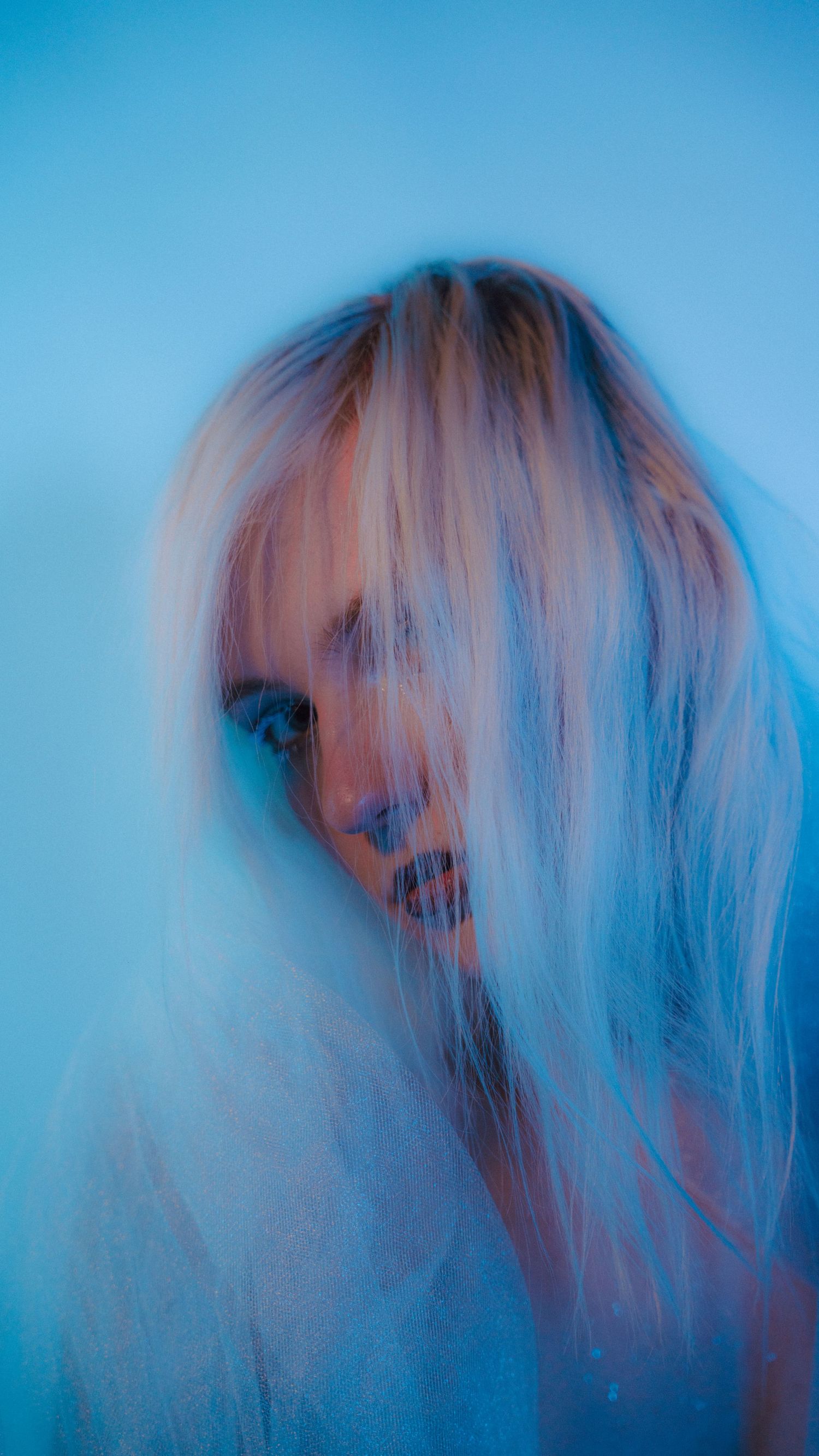 A woman with long blonde hair poses in a dreamy blue-tinted portrait with artistic motion blur effect.