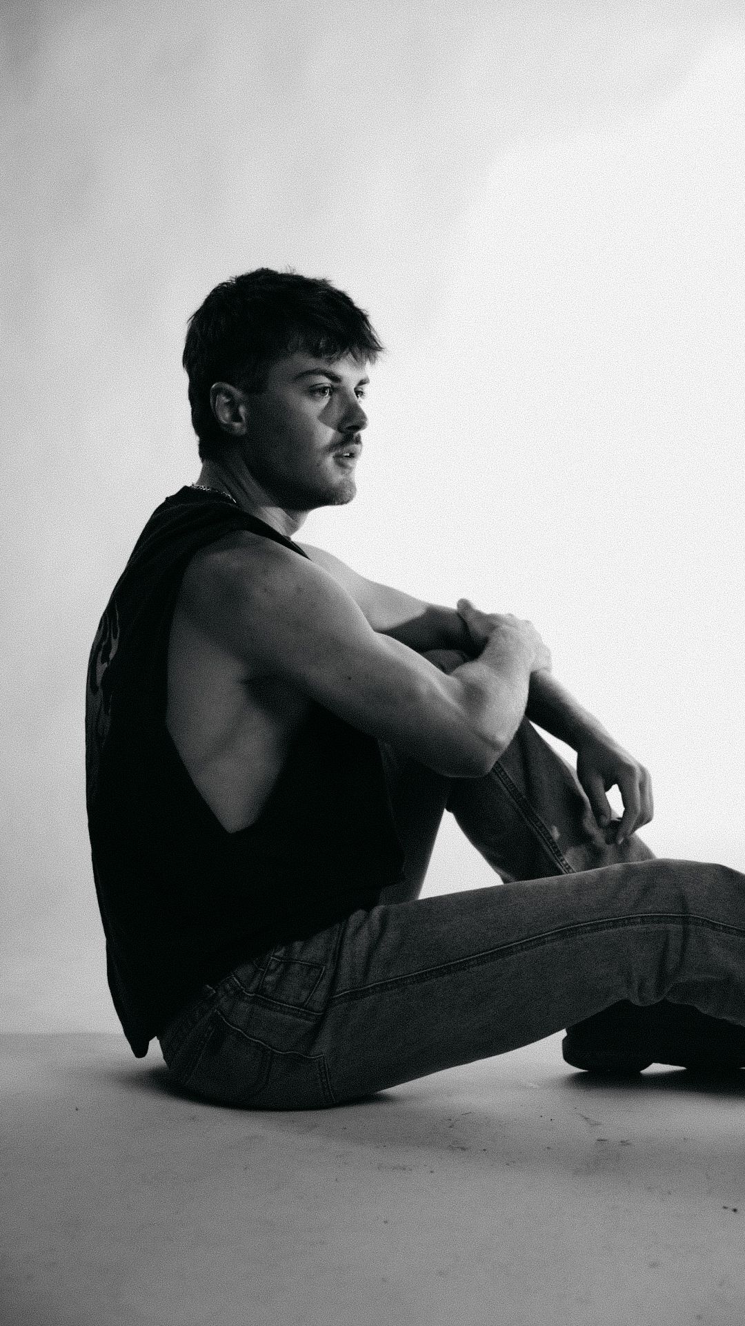 Athletic man in black tank top sitting on floor in black and white photo.