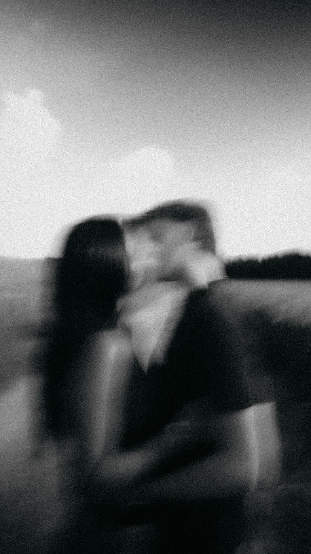 Blurry black and white photo of a couple kissing in a field, creating a dreamy, romantic motion blur effect.