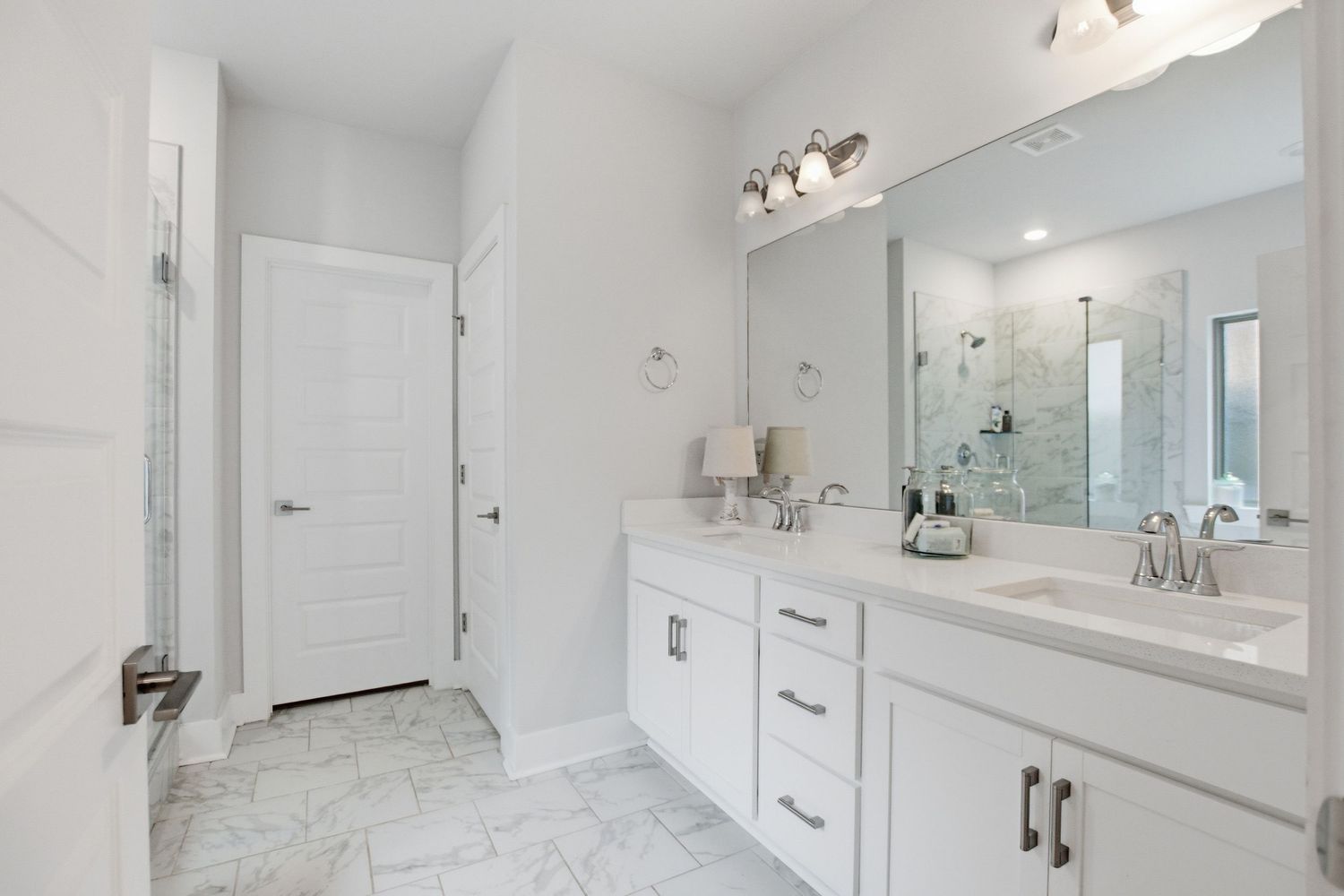 Double vanity bathroom with white cabinets, marble tile floors, large mirror, and glass shower.