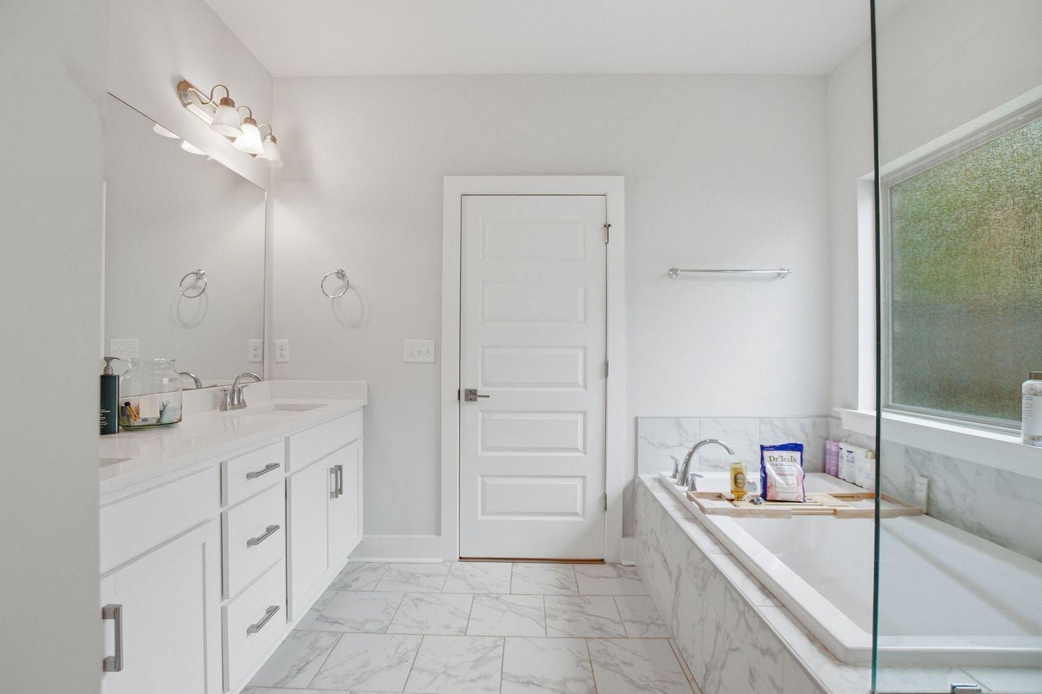 Luxurious master bathroom with double vanity, soaking tub, marble tile floors, and large window for natural light.