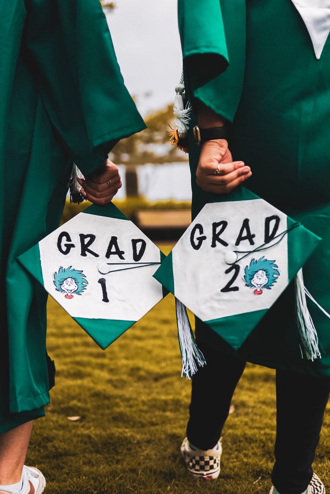 Two graduates in green caps and gowns holding mortarboards labeled Grad 1 and Grad 2.