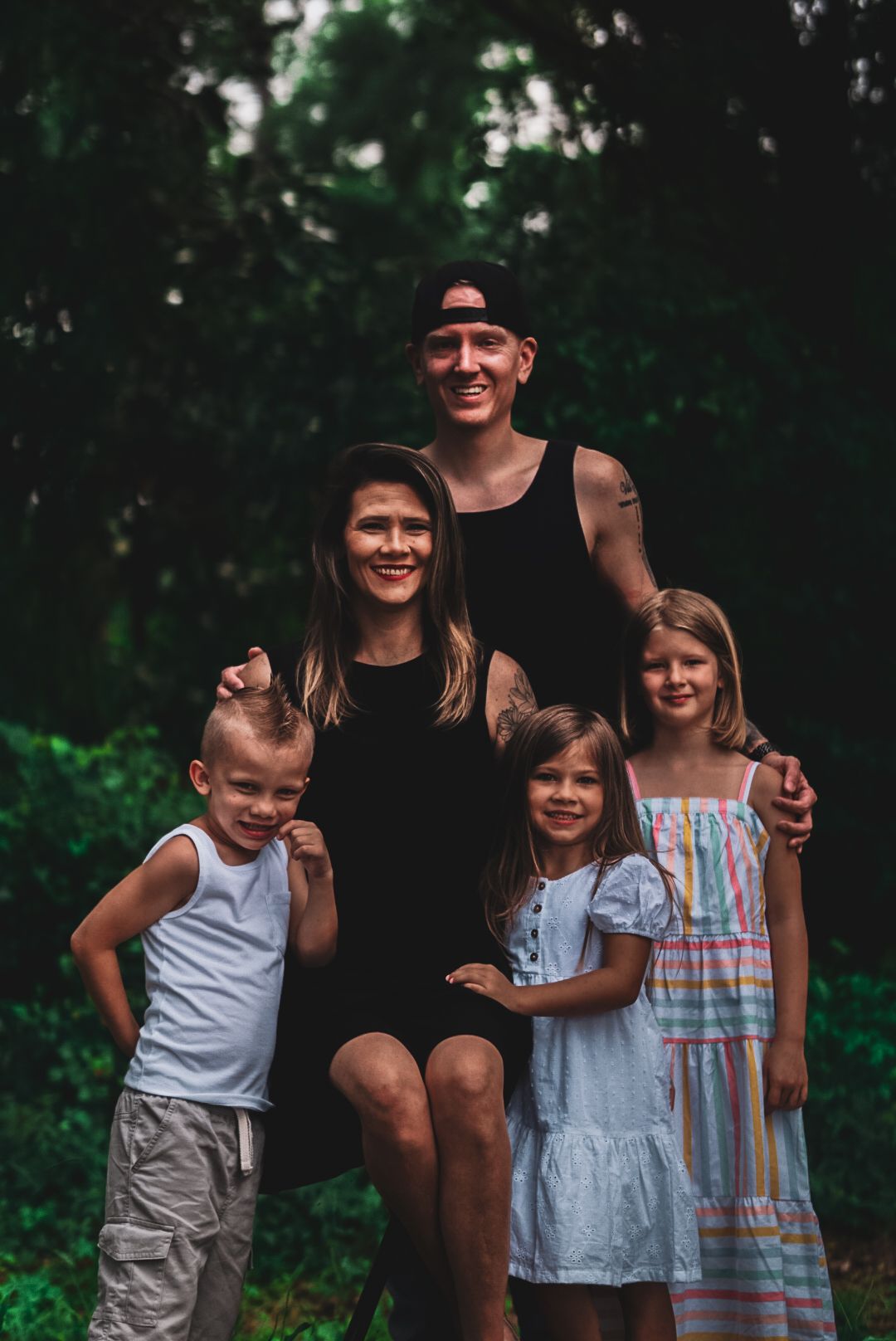 Happy family of five posing together in a lush green forest setting.