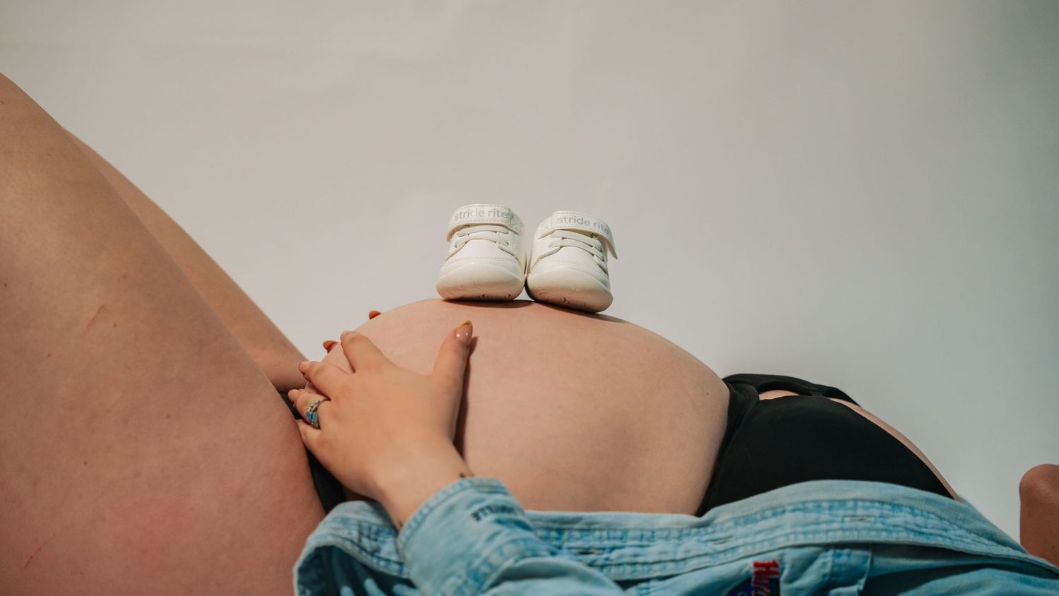 Pregnant woman resting with tiny white baby shoes balanced on her baby bump, symbolizing upcoming motherhood.