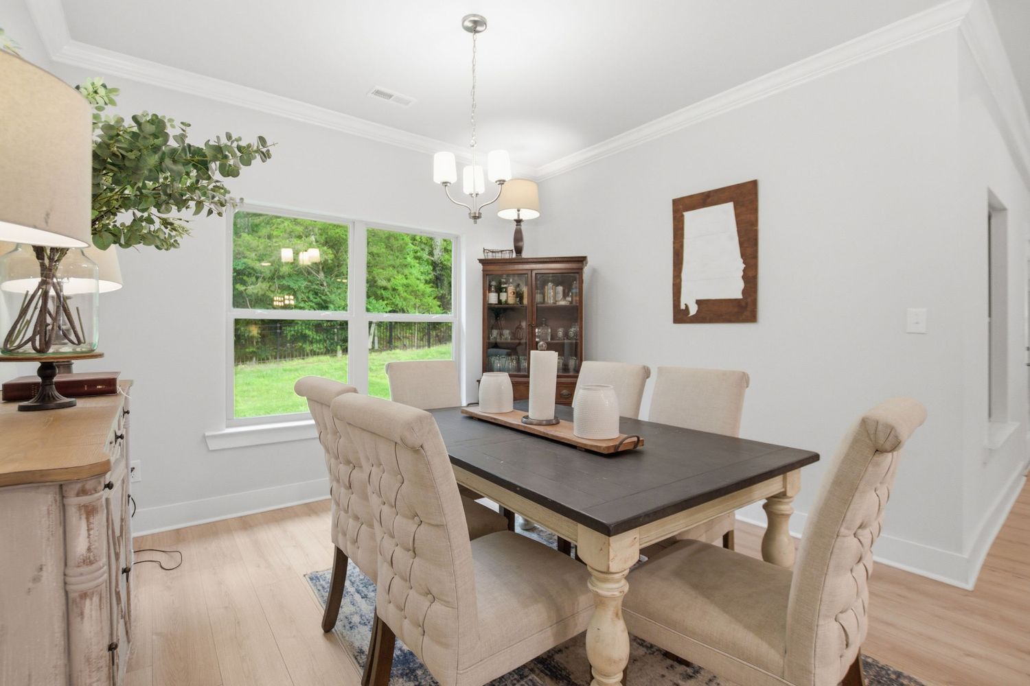 Bright dining room with farmhouse table, tufted chairs, hardwood floors, crown molding, and a chandelier near large windows.