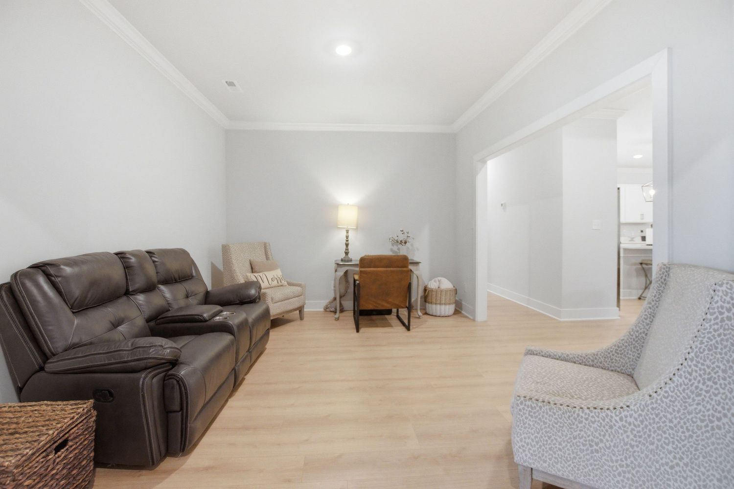 Bright living room with brown leather recliner sofa, light hardwood floors, crown molding, and neutral gray walls.