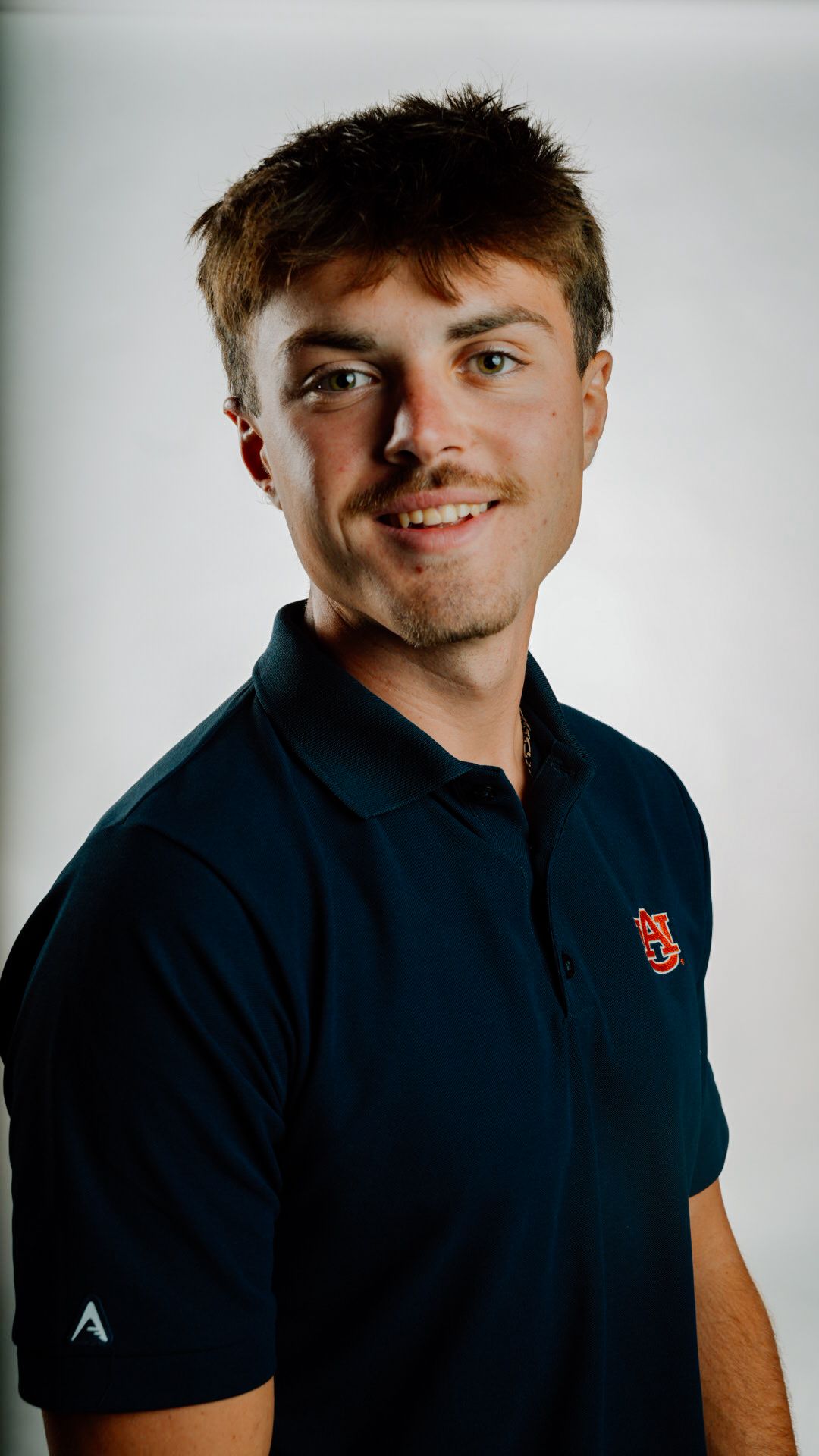 Young man smiling in navy Auburn University polo shirt against white background, professional headshot photo.